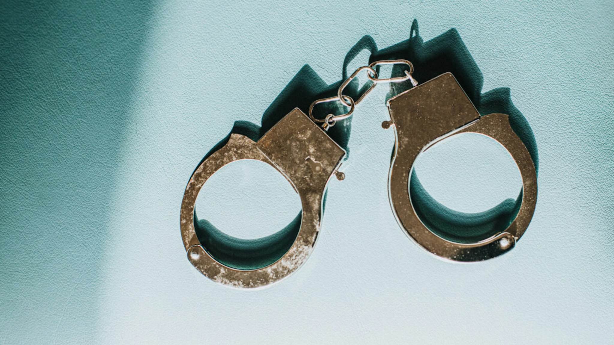 Shiny silver metal handcuffs on blue surface with space for copy.