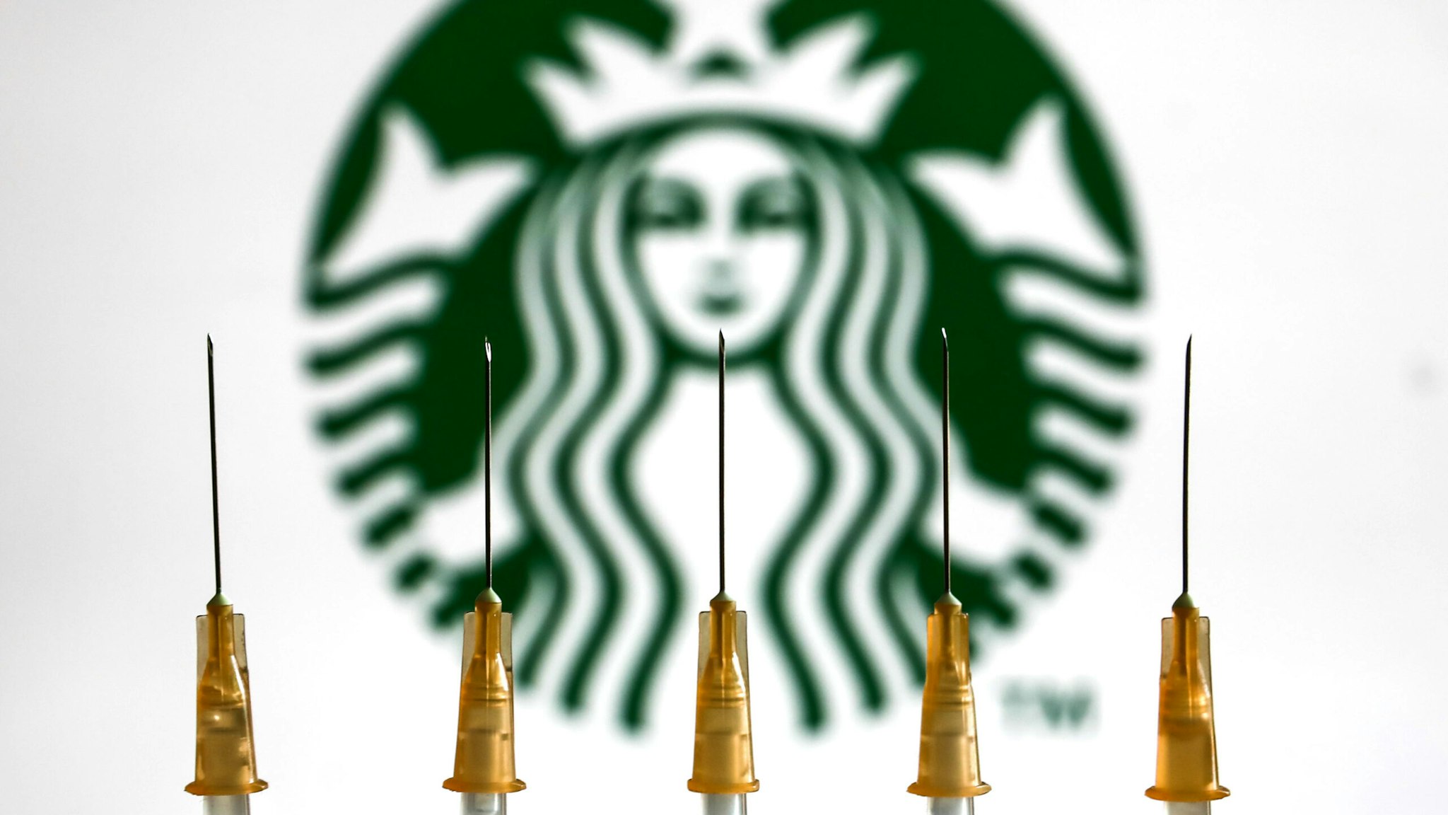 Medical syringes and Starbucks logo displayed in the background are seen in this illustration photo taken in Krakow, Poland on January 11, 2022.