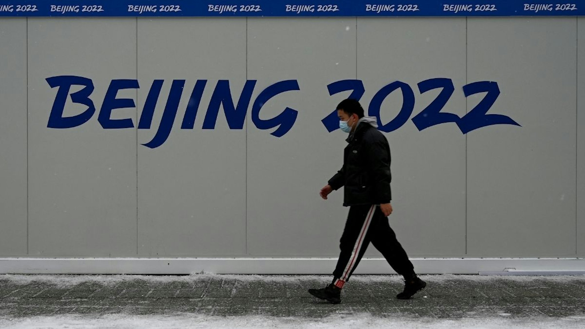 A man walks past a promotion for the 2022 Beijing Winter Olympic Games, at the Olympic Park, two weeks before the start of the 2022 Beijing Winter Olympic Games, on a snowy day in Beijing on January 20, 2022.