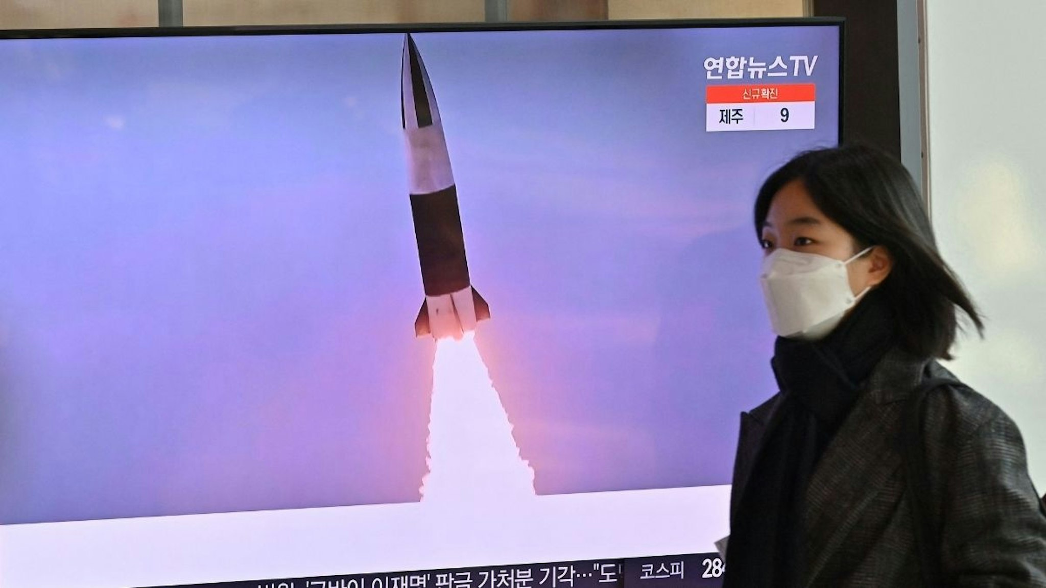 A woman walks past a television screen showing a news broadcast with file footage of a North Korean missile test, at a railway station in Seoul on January 20, 2022, after North Korea hinted it could resume nuclear and long-range weapons tests, as it prepared for "long-term confrontation" with the United States, following a string of sanction-busting missile launches this month.