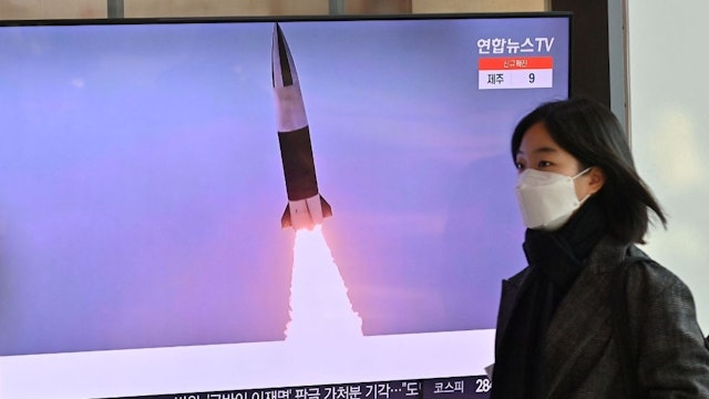 A woman walks past a television screen showing a news broadcast with file footage of a North Korean missile test, at a railway station in Seoul on January 20, 2022, after North Korea hinted it could resume nuclear and long-range weapons tests, as it prepared for "long-term confrontation" with the United States, following a string of sanction-busting missile launches this month.