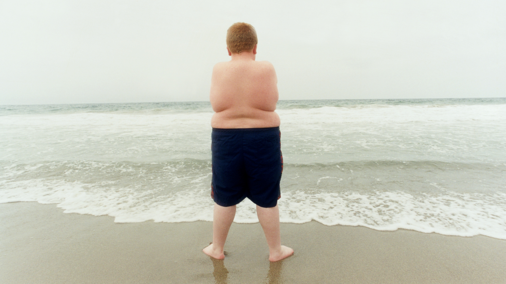 Overweight boy (10-12) standing on beach- stock photo Zuma Beach, Malibu, California, USA.