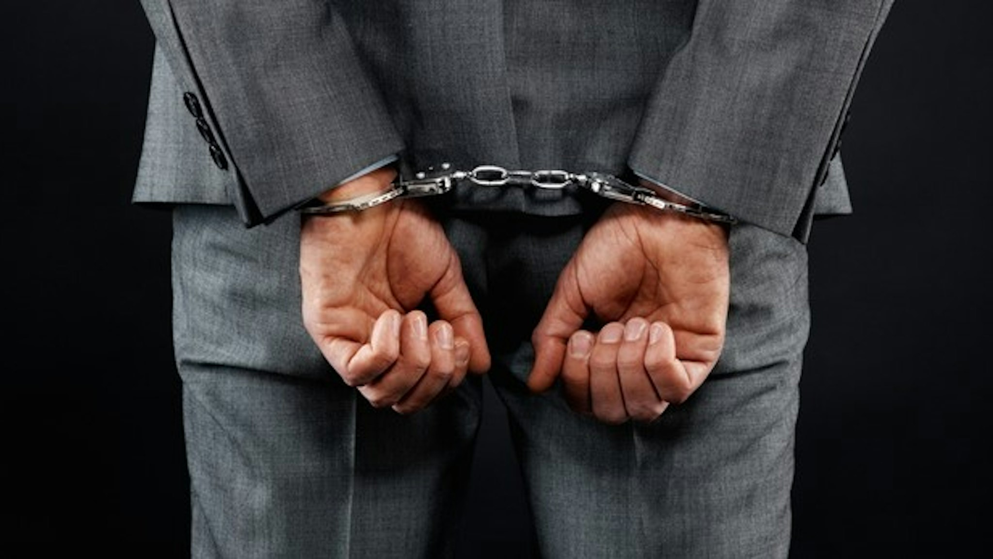 Rear view of man in suit wearing handcuffs
