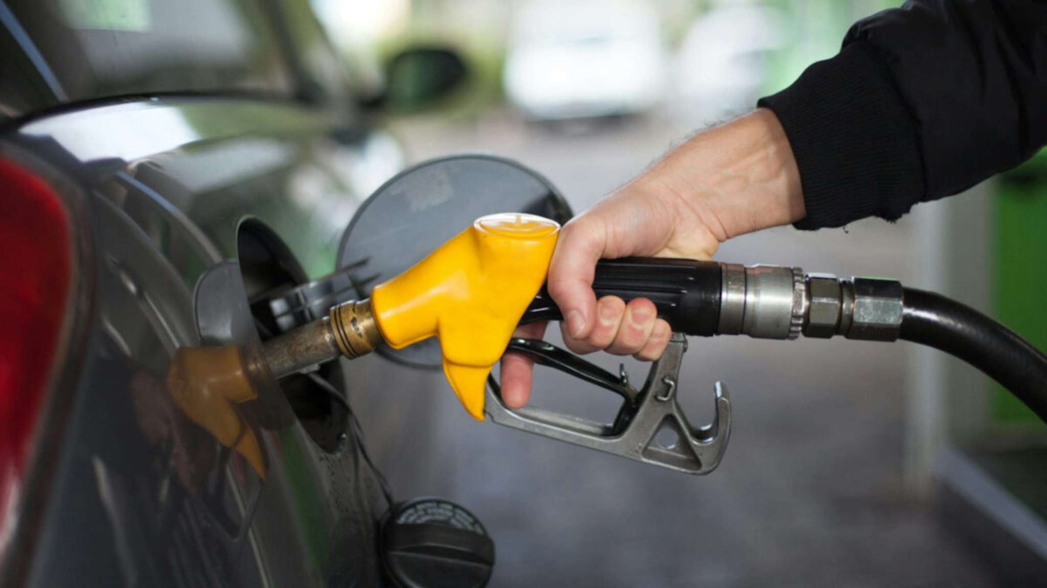 Hand of man fueling up a vehicle with a yellow gas pump.