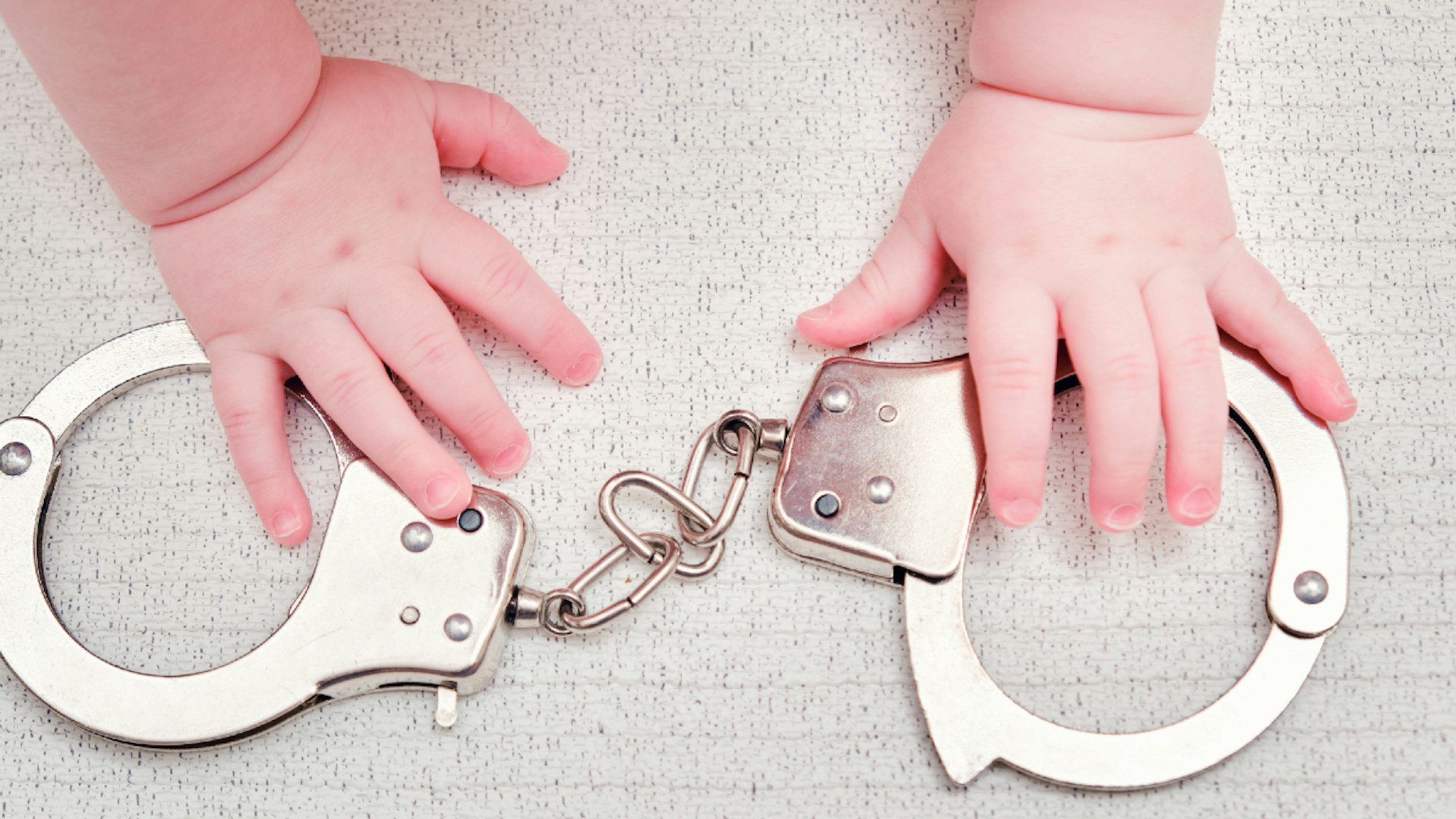 Baby hand and handcuffs, close-up. Children fingers and an object on a white background