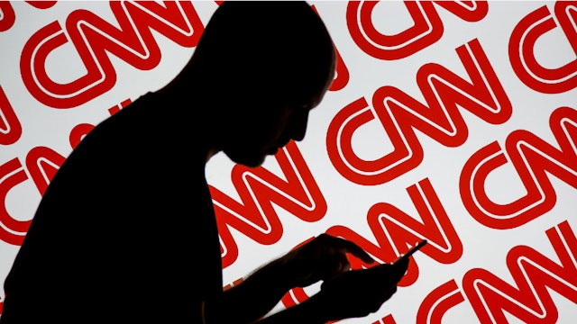 A man is seen holding with a smart device in front of a CNN logo in this photo illustration on 2 July, 2017.