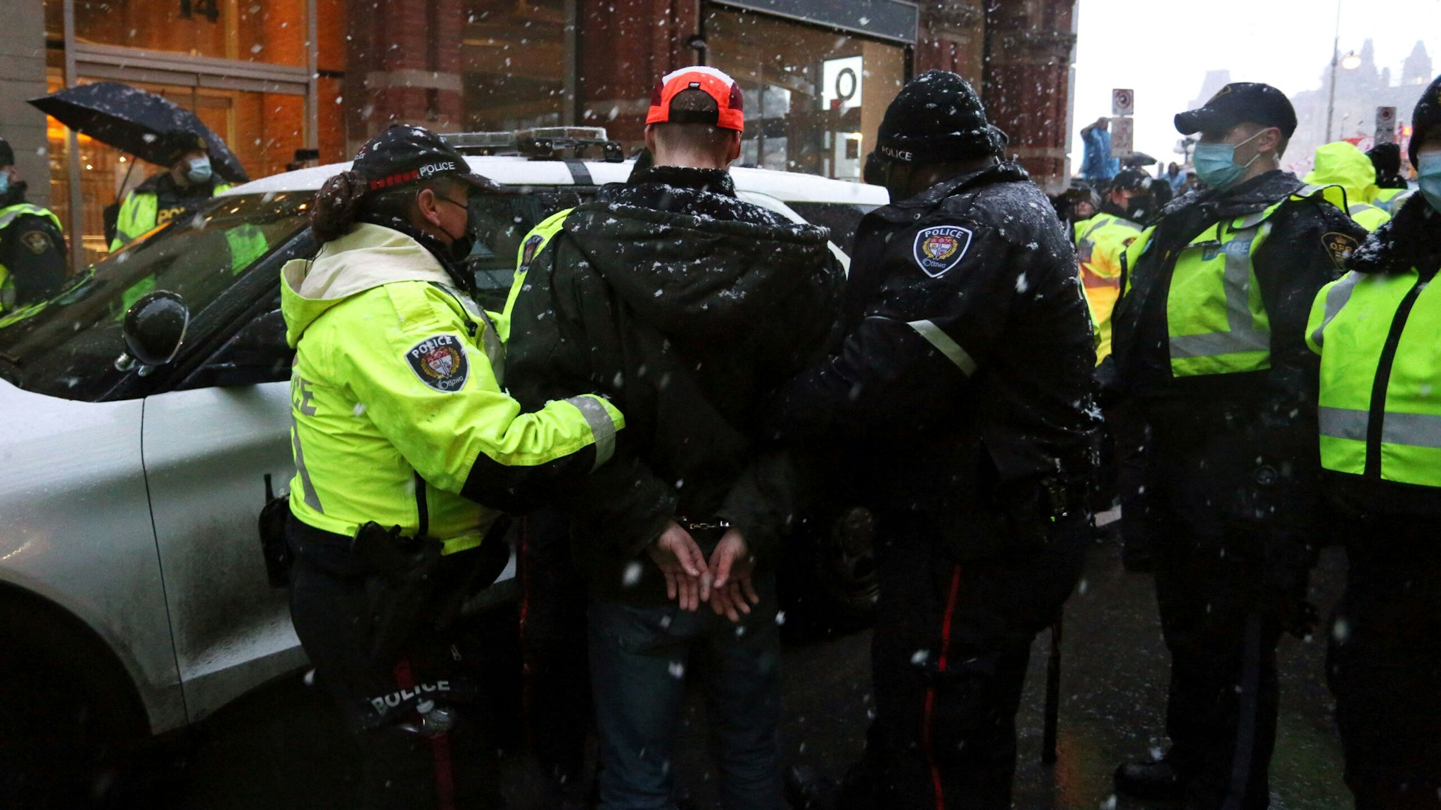 TOPSHOT - Police officers escort an arrested protester to a police car during a protest over pandemic health rules and the Trudeau government in Ottawa, Canada on February 17, 2022. - Canadian police massed in the capital February 17, 2022, readying to clear a trucker-led protest that has choked Ottawa's streets for three weeks and provoked the government to call on rarely used emergency powers.