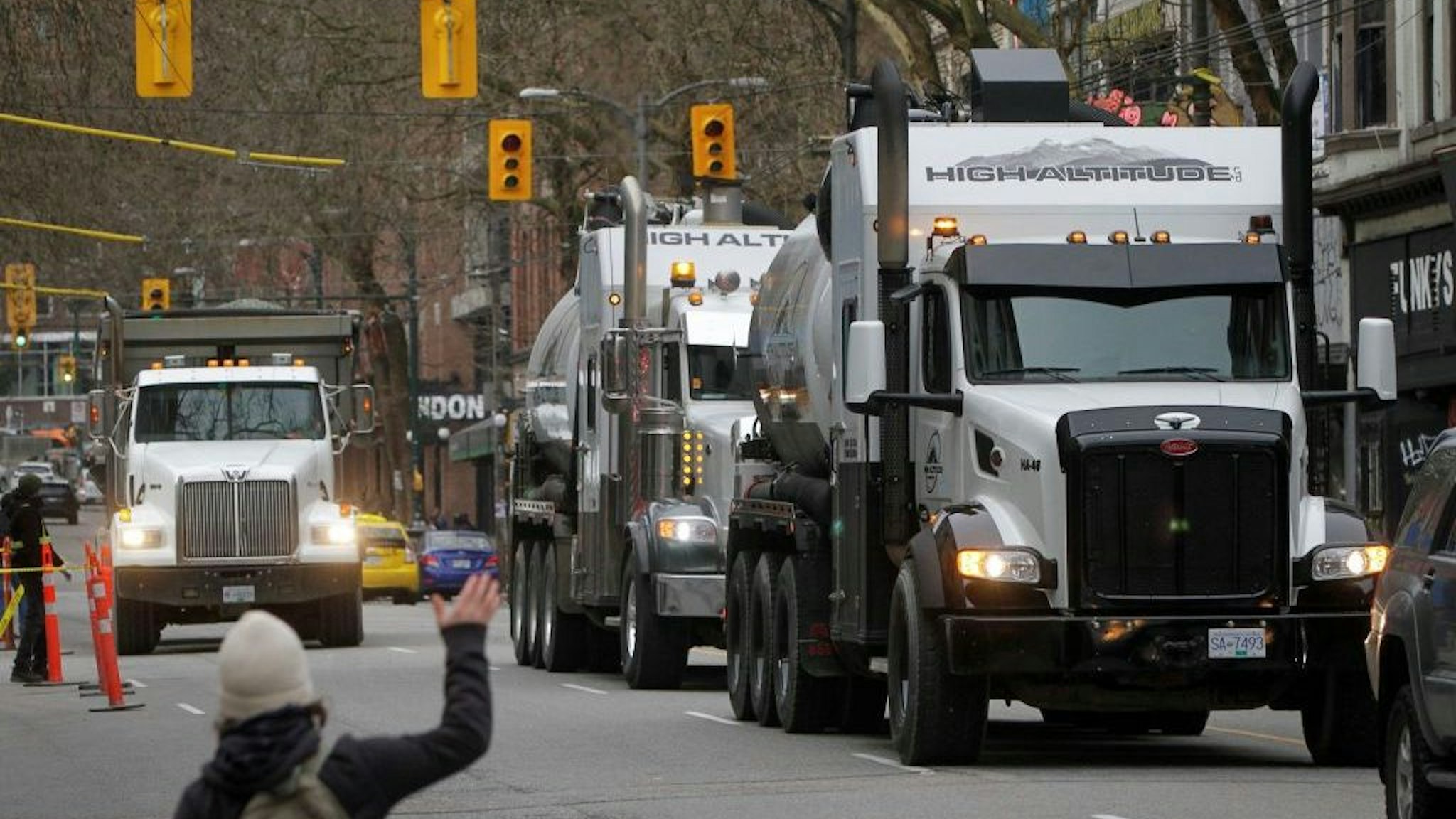 A person gestures to vehicles on the street during a parade in support of Ottawa's "Freedom Convoy" trucker protest in downtown Vancouver, British Columbia, Canada, Jan. 29, 2022. Vehicles jammed downtown Vancouver streets Saturday to show their support of the "Freedom Convoy" of long-haul drivers to oppose the Canadian government's requirement that all cross-border essential workers, including truckers, must show proof of vaccination at a port of entry. (Photo by Liang Sen/Xinhua via Getty Images)