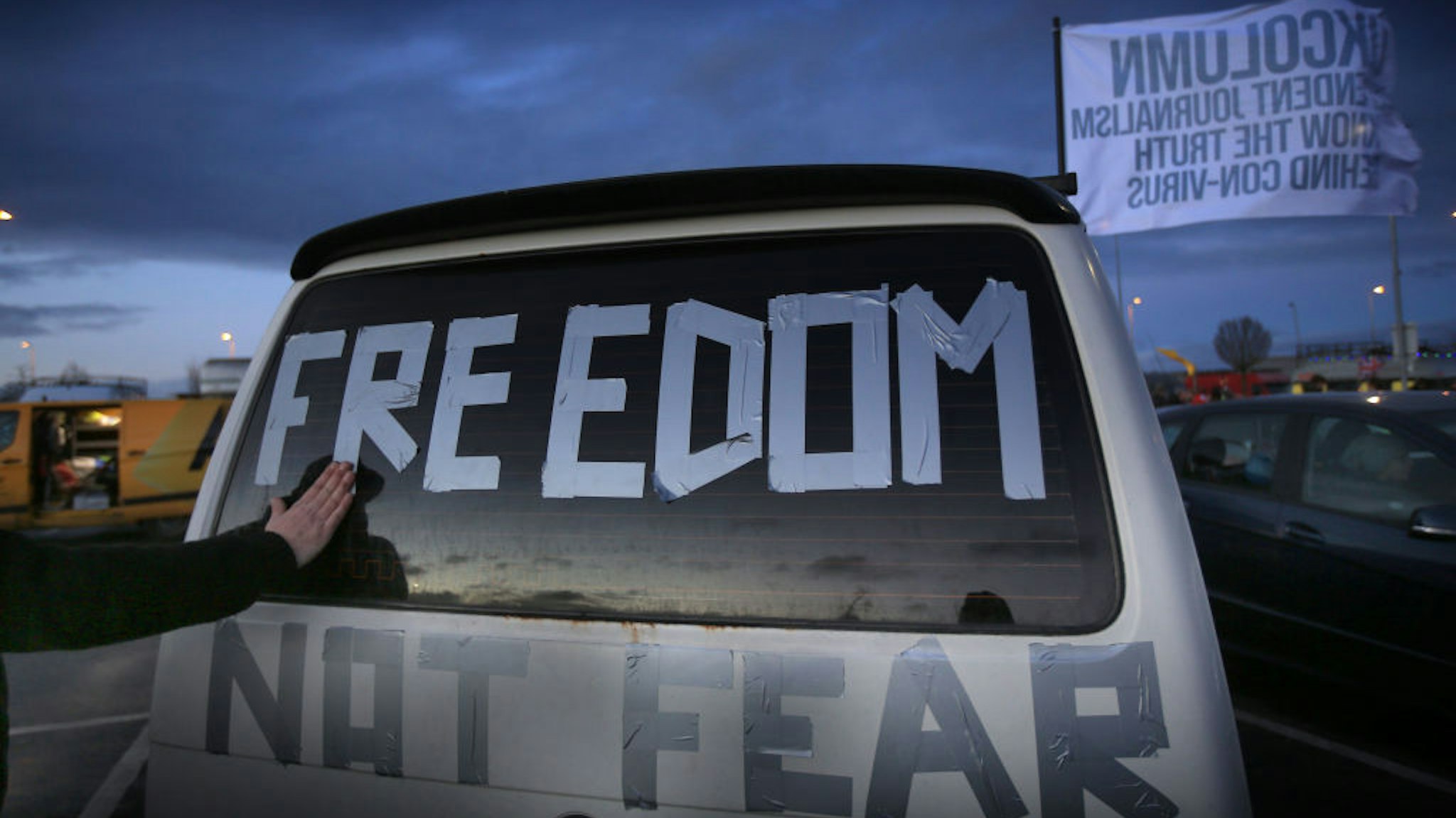 A protester tapes a Freedom not fear message on the back of his car at Cobham services on the M25 as protesters welcome fellow members of the convoy as they arrive on February 6, 2022 in Cobham, England.