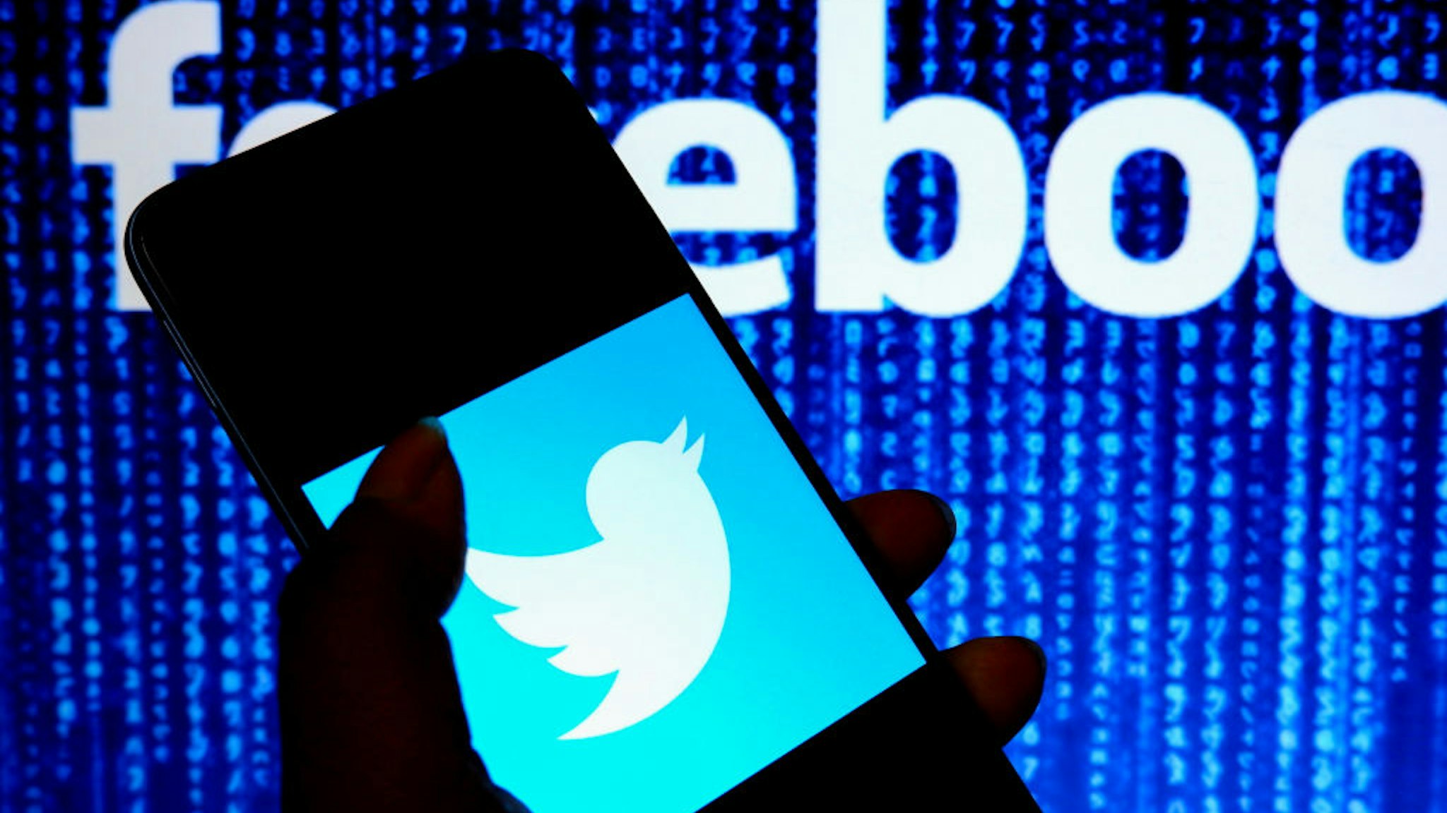 In this photo illustration, a Twitter logo is displayed on a smartphone screen with a Facebook logo in the background.