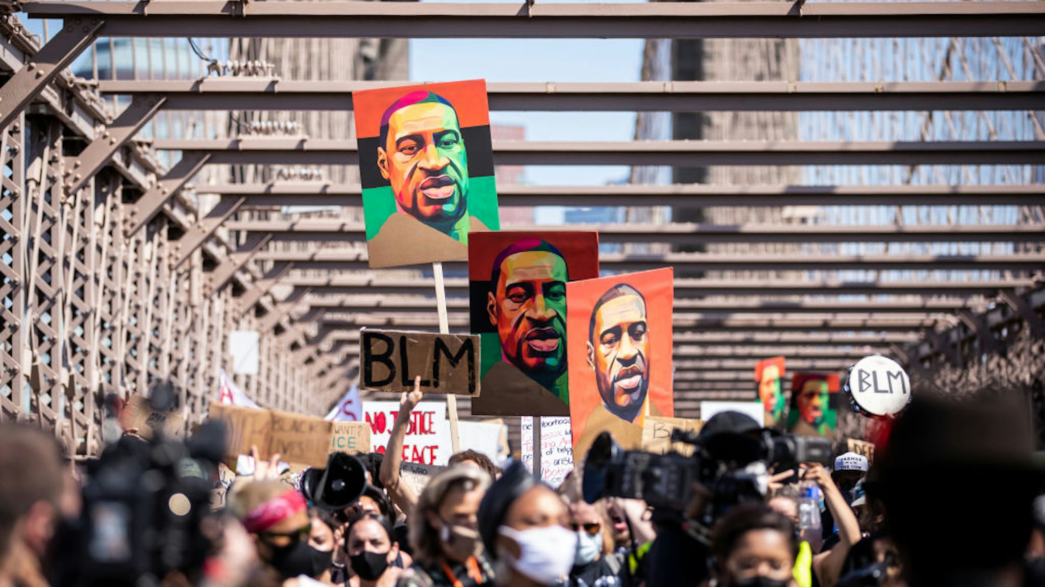 MANHATTAN, NY - JUNE 19: Thousands of protesters walk in a peaceful protest across the Brooklyn Bridge holding signs that read, "BLM" and three painted portraits of George Floyd with the Brooklyn Bridge Arch in the background. This was part of the Unite NY 2020, Bringing all of New York Together rally and march as protests that happened around the country to celebrate Juneteenth day which marks the end of slavery in the United States. Protesters continue taking to the streets across America and around the world after the killing of George Floyd at the hands of a white police officer Derek Chauvin that was kneeling on his neck during for eight minutes, was caught on video and went viral. During his arrest as Floyd pleaded, "I Can't Breathe". The protest are attempting to give a voice to the need for human rights for African American's and to stop police brutality against people of color. They are also protesting deep-seated racism in America. Many people were wearing masks and observing social distancing due to the coronavirus pandemic. Photographed in the Manhattan Borough of New York on June 19, 2020, USA.