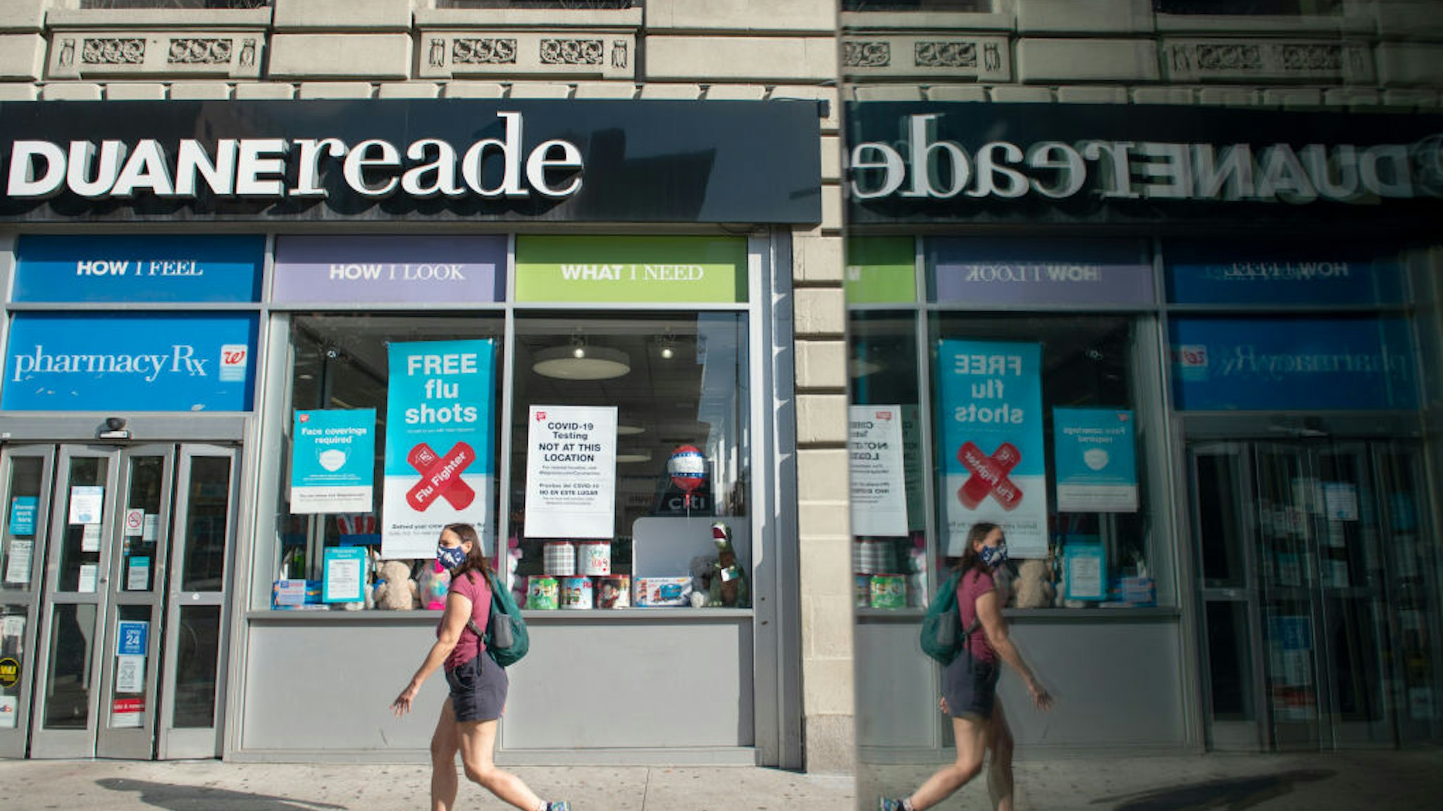 NEW YORK, NEW YORK - SEPTEMBER 28: A woman wearing a mask walks past a Duane Reade pharmacy near a LinkNYC screen creating a reflection as the city continues Phase 4 of re-opening following restrictions imposed to slow the spread of coronavirus on September 28, 2020 in New York City. The fourth phase allows outdoor arts and entertainment, sporting events without fans and media production. (Photo by Alexi Rosenfeld/Getty Images)