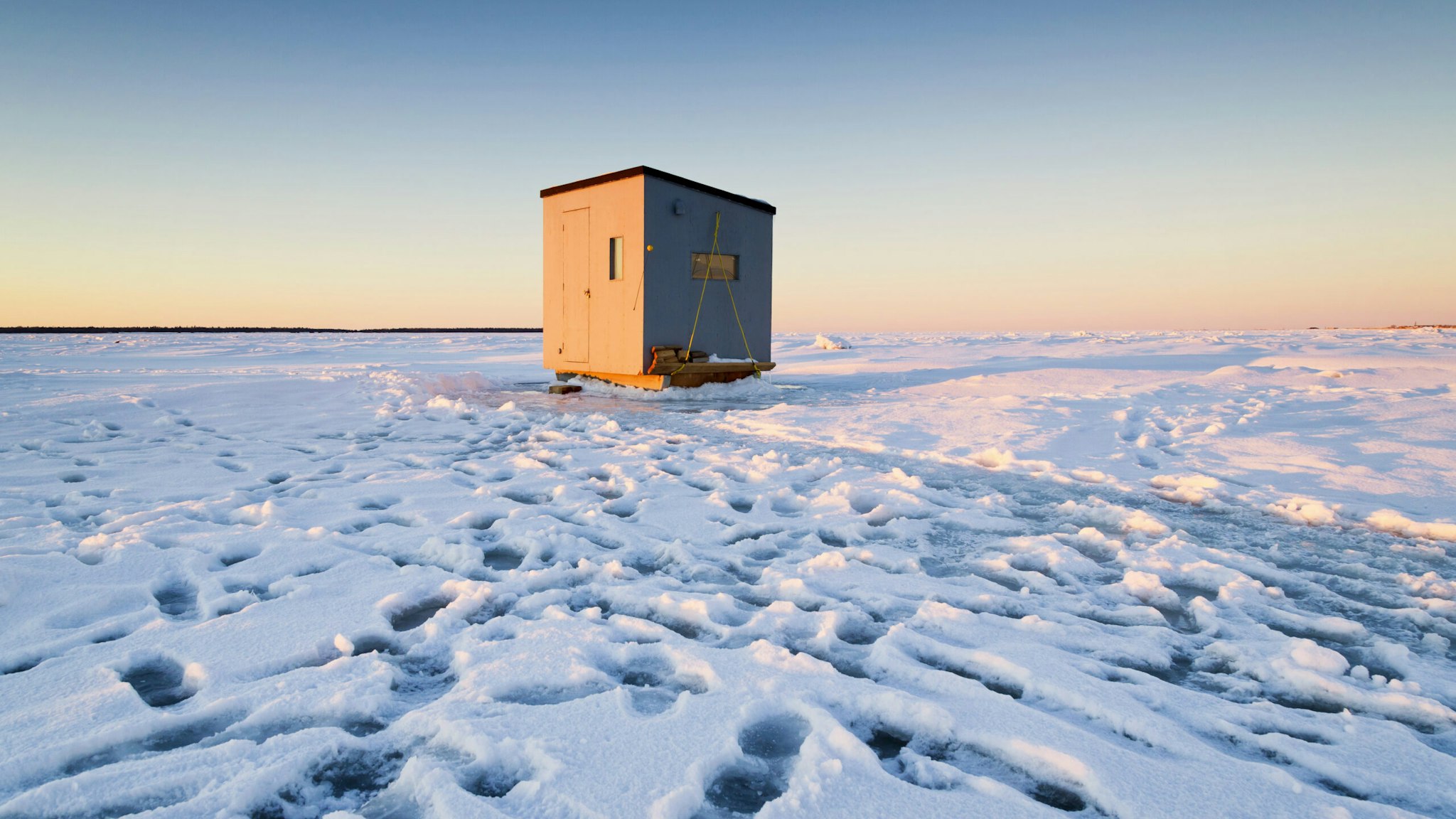 Les promeneurs ont laissé des empreintes de pas dans la neige et sur la galce autour d'une cabane de pêche blanche installée sur la banquise dans la baie de Rimouski (MRC de Rimouski-Neigette, Bas-Saint-Laurent, Québec).