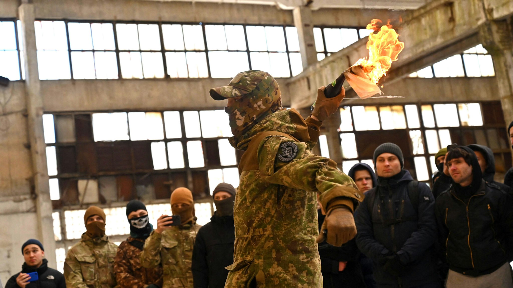 TOPSHOT - A military instructor teaches civilians to use Molotov cocktails during a training session at an abandoned factory in the Ukrainian capital of Kyiv on February 6, 2022. - Amid fears of a potential invasion by Russian troops massed on Ukraine's border, within the framework of the training there were classes on tactics, paramedics, training on the obstacle course. The training is conducted by instructors with combat experience, members of the movement "Total Resistance". Ukraine's presidency on February 06, insisted the chance of resolving soaring tensions with Russia through diplomacy remained greater than that of an attack, as the US warned Moscow was stepping up preparations for an invasion. "An honest assessment of the situation suggests that the chance of finding a diplomatic solution for de-escalation is still substantially higher than the threat of further escalation," said presidency advisor Mykhailo Podolyak in a statement.