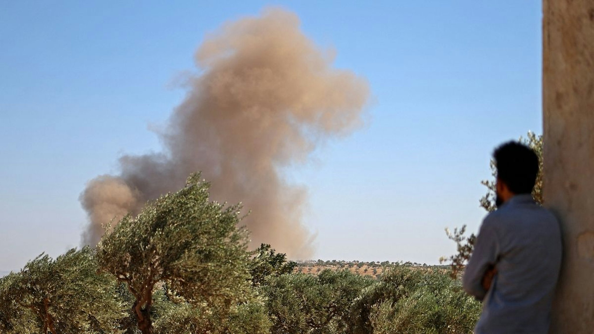 A Syrian man looks on as a plume of smoke rises in the distance, caused by reported airstrikes by pro-regime forces, north of the rebel-held city of Idlib, on August 20, 2021.