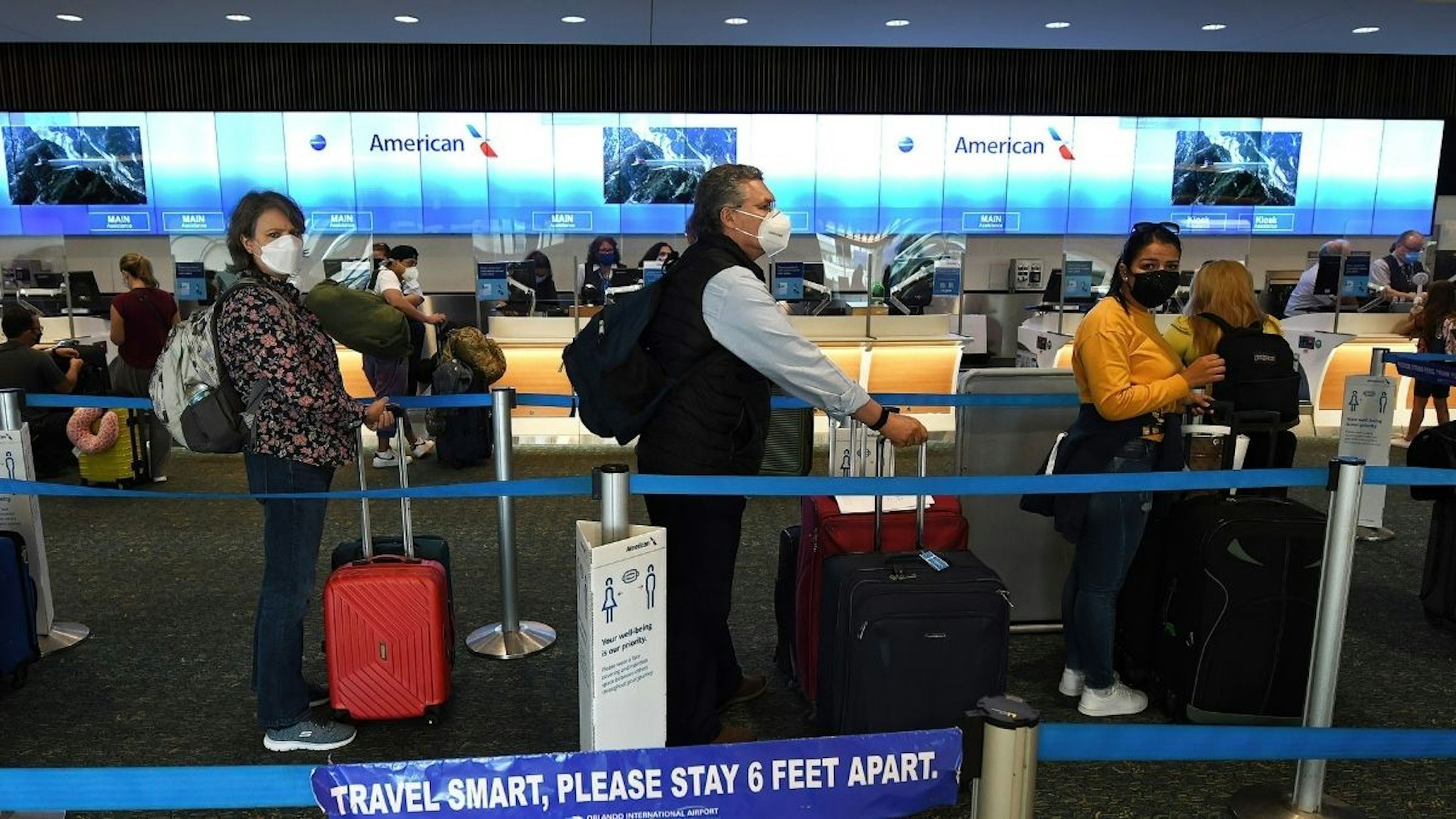 Travelers wearing face masks as a preventive measure against the spread of covid-19 wait in line at the American Airlines ticket counter at Orlando International Airport.