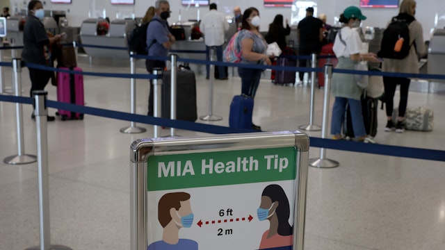 A sign advises people to wear a mask and stand 6 ft apart as travelers make their way through Miami International Airport on December 28, 2021 in Miami, Florida.