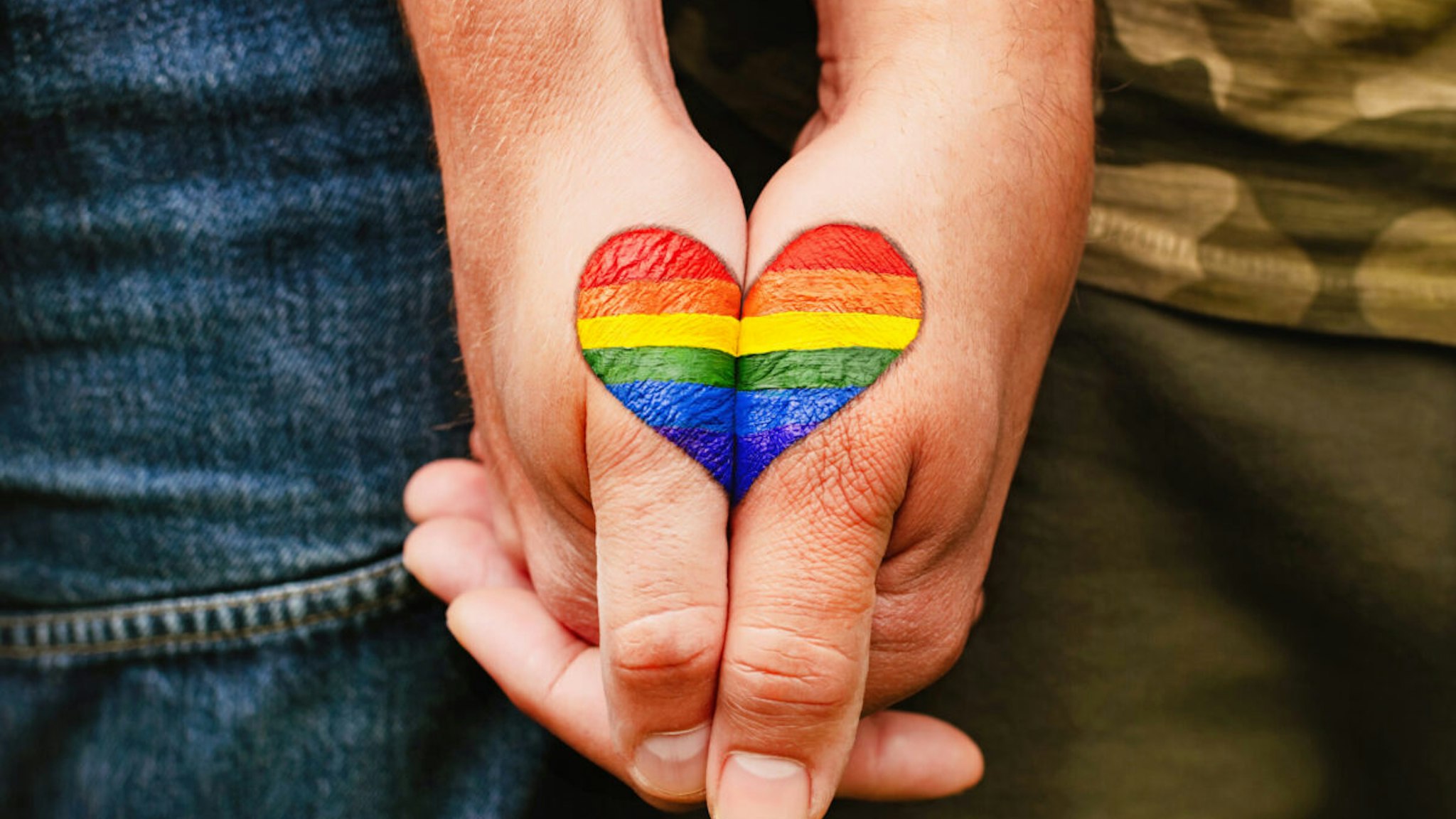 Rainbow heart drawing on hands, LGBTQ love symbol, gay couple hand in hand, homoseaxual lovers