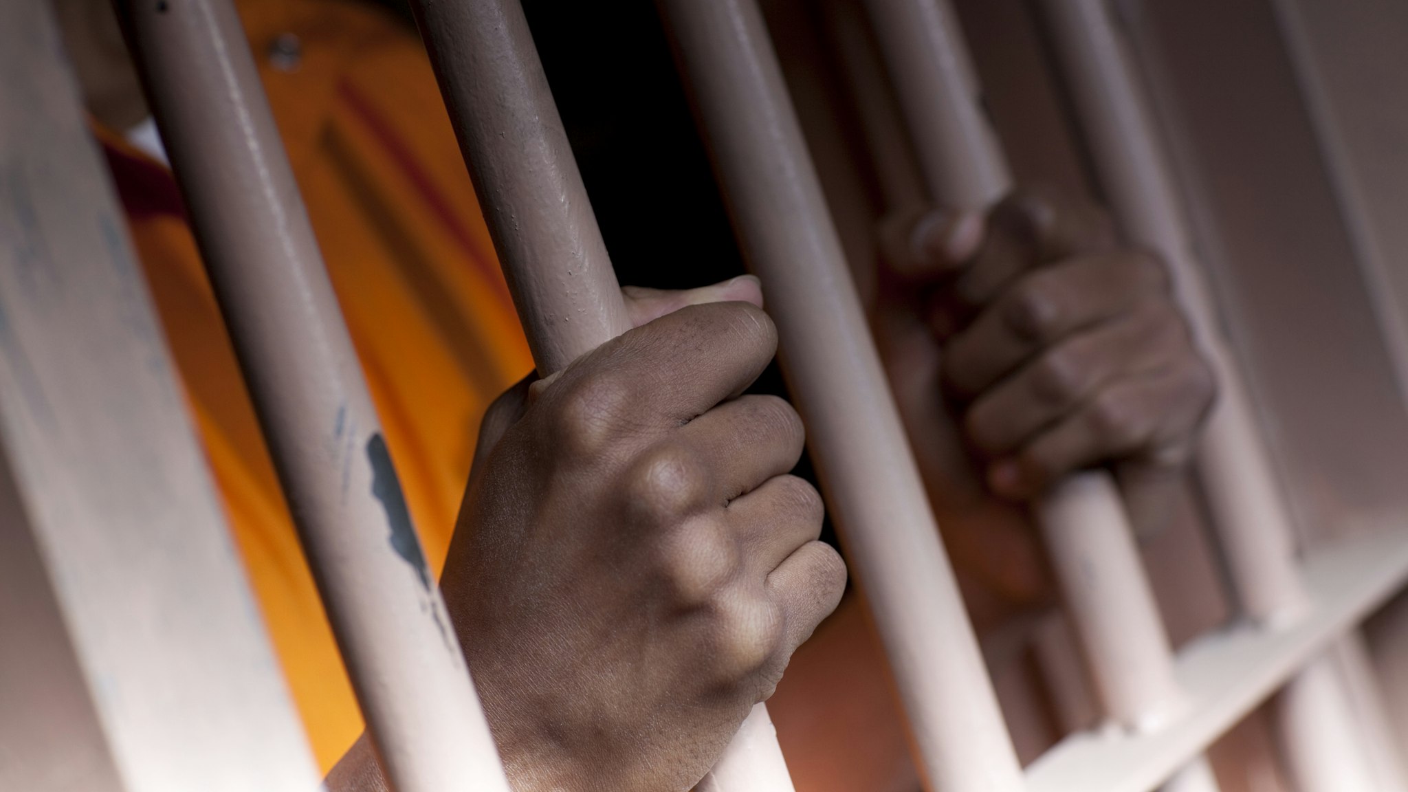 A black man with hands outside the bars of a prison cell