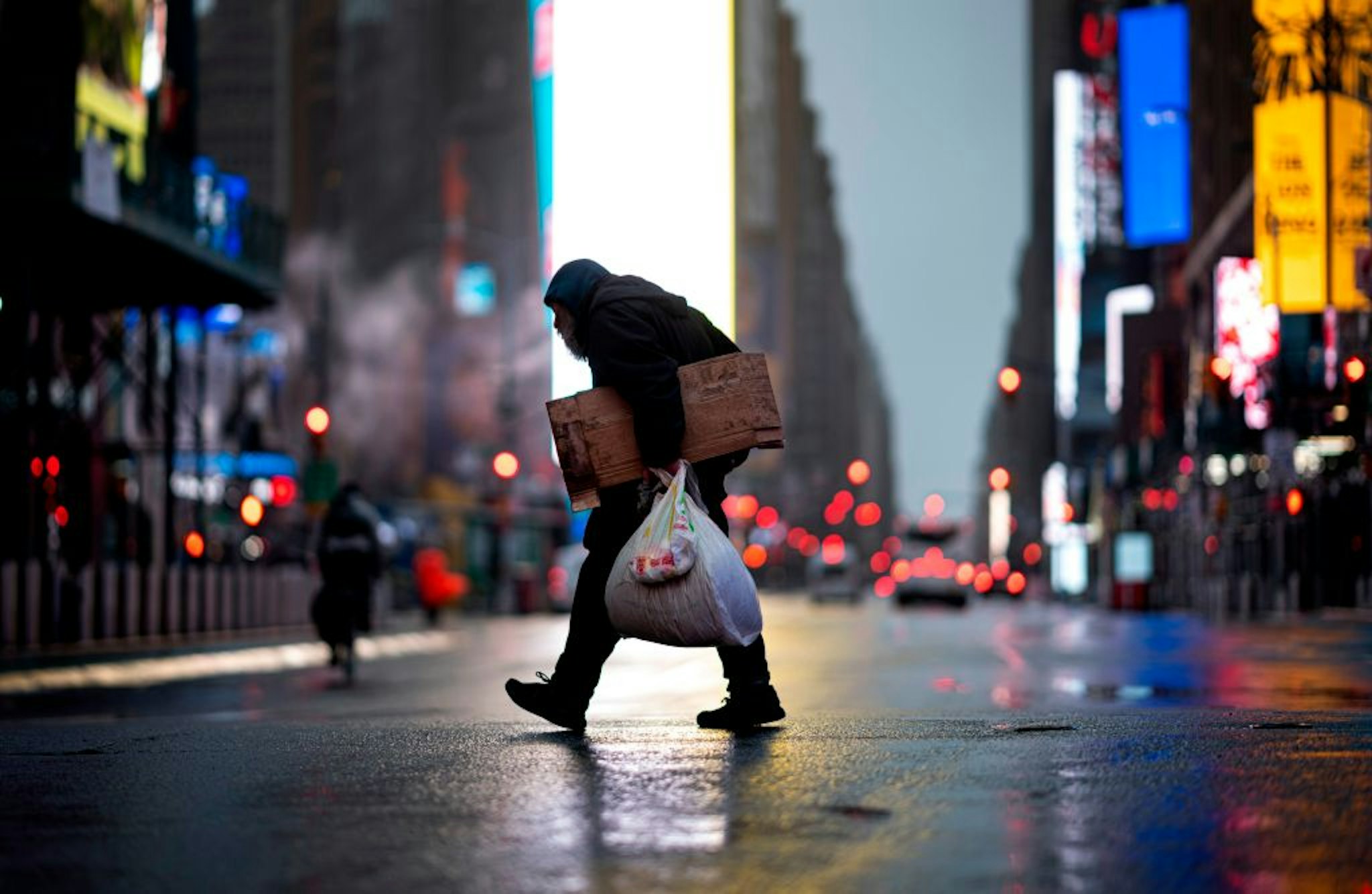 A homeless man carries cardboard as he crosses the almost deserted Times Square on April 13, 2020 in New York City. - New York's governor declared April 13, 2020 that the "worst is over" for its coronavirus outbreak providing the state moves sensibly, despite reporting its death toll had passed 10,000. Andrew Cuomo said lower average hospitalization rates and intubations suggested a "plateauing" of the epidemic and that he was working on a plan to gradually reopen the economy. (Photo by Johannes EISELE / AFP) (Photo by JOHANNES EISELE/AFP via Getty Images)