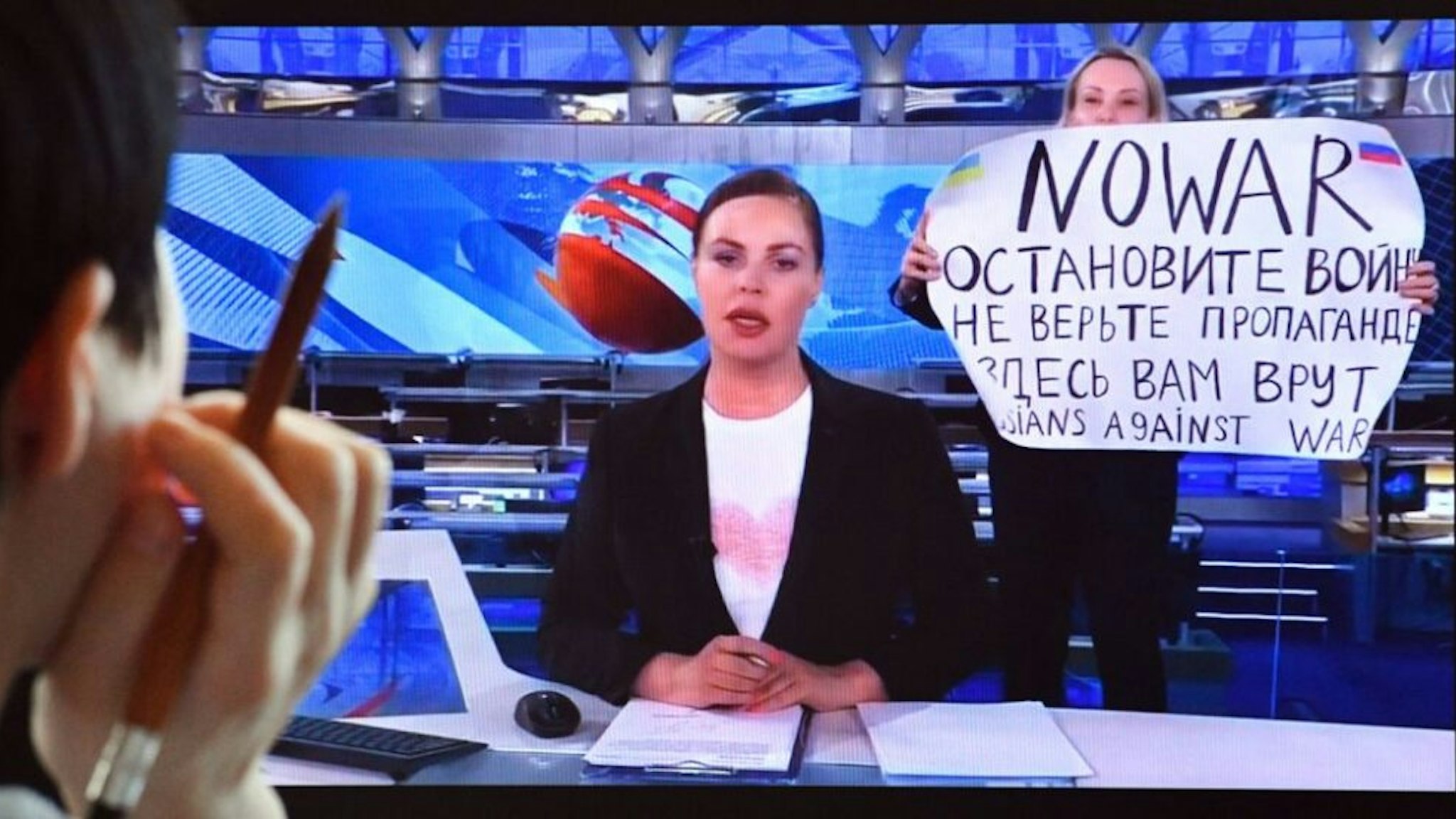 A woman looks at a computer screen watching a dissenting Russian Channel One employee entering Ostankino on-air TV studio during Russia's most-watched evening news broadcast, holding up a poster which reads as "No War" and condemning Moscow's military action in Ukraine in Moscow on March 15, 2022. - As a news anchor Yekaterina Andreyeva launched into an item about relations with Belarus, Marina Ovsyannikova, who wore a dark formal suit, burst into view, holding up a hand-written poster saying "No War" in English.
