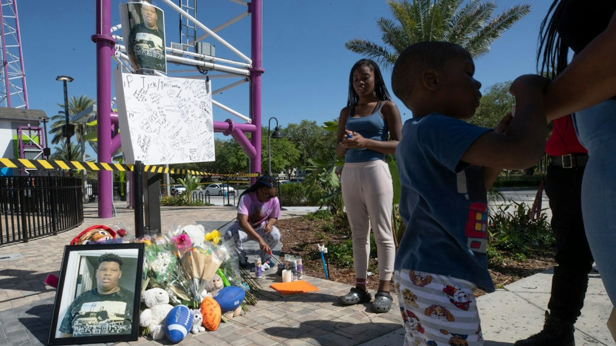 Visitors stand next to the memorial while a family member lights candles for Tyre Sampson, 14, who was killed when he fell from the Orlando Free Fall ride at ICON Park in Orlando, Florida, on Saturday, March 26, 2022.