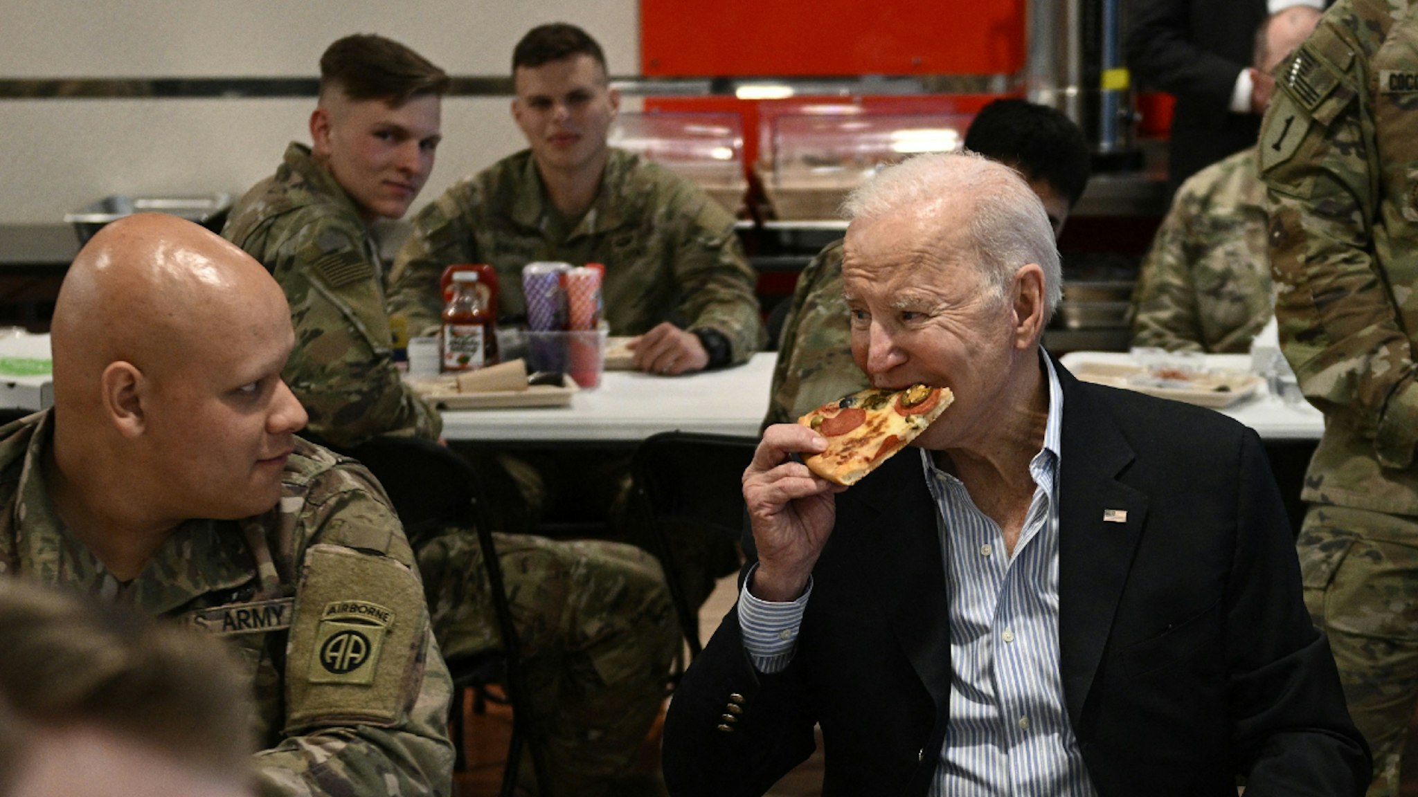 US President Joe Biden (C) eats a pizza as he meets with service members from the 82nd Airborne Division, who are contributing alongside Polish Allies to deterrence on the Alliances Eastern Flank, in the city of Rzeszow in southeastern Poland, around 100 kilometres (62 miles) from the border with Ukraine, on March 25, 2022.
