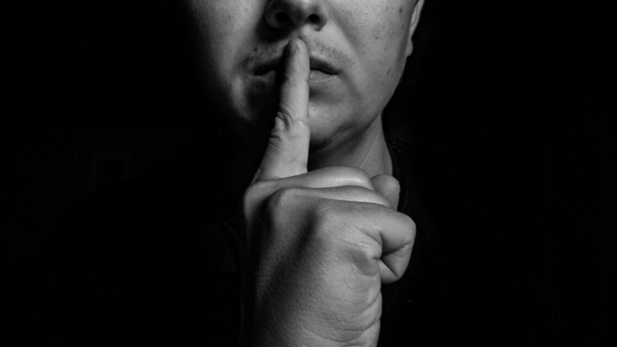 Close-Up Of Man With Finger On Lips Against Black Background