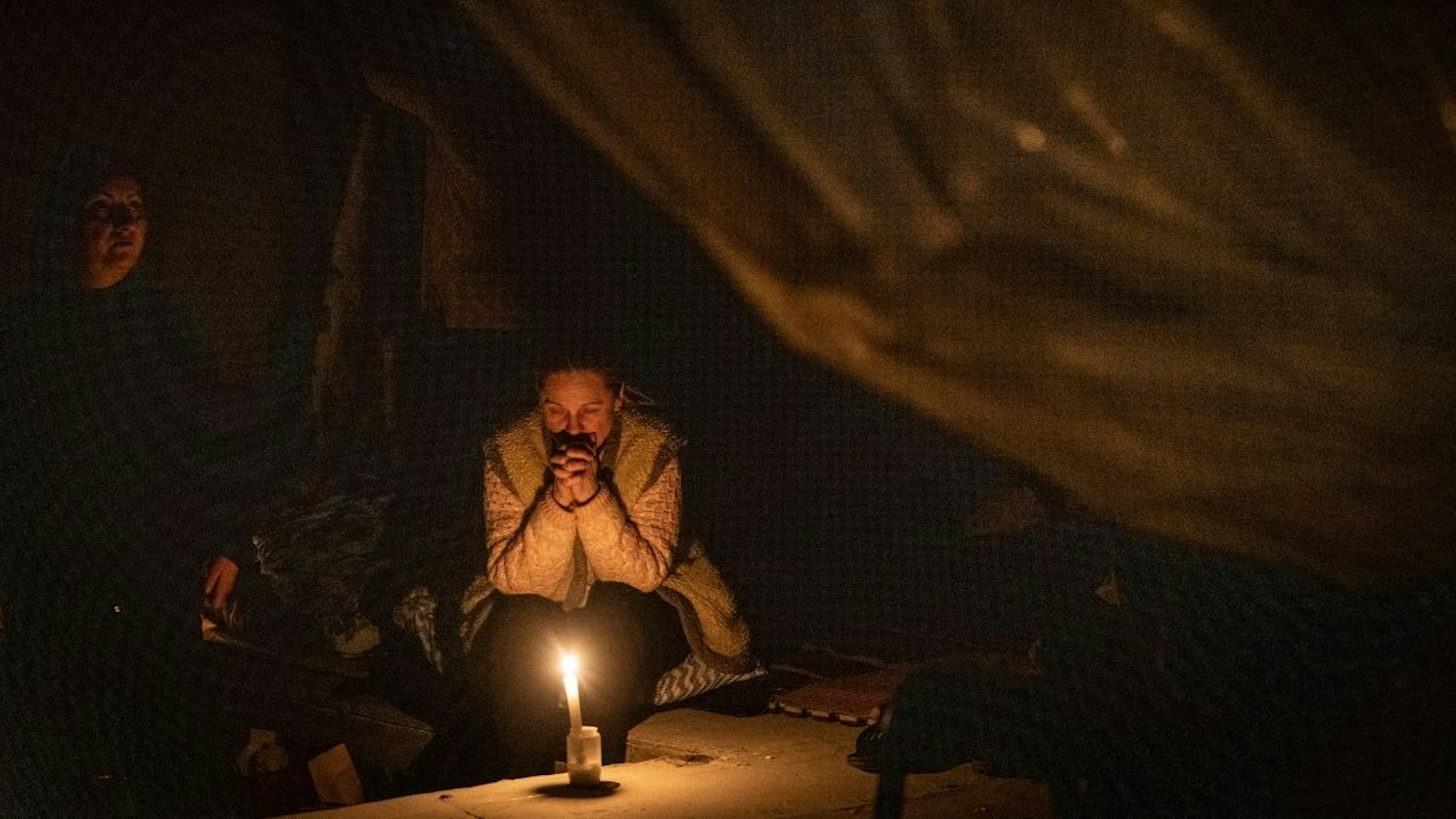 A resident prays while sheltering in by candle light in the basement of a building in Irpin as Russian forces moved through the city on March 07, 2022 in Irpin, Ukraine.