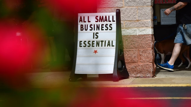 A man walks his dog past a placard stating "ALL SMALL BUSINESS IS ESSENTIAL" outside Atilis Gym on May 20, 2020 in Bellmawr, New Jersey.