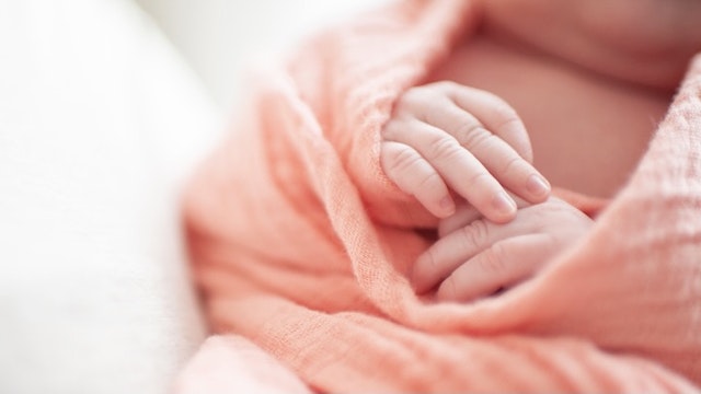 Close up of newborn baby girls hands wrapped in pink blanket - stock photo Cavan Images via Getty Images