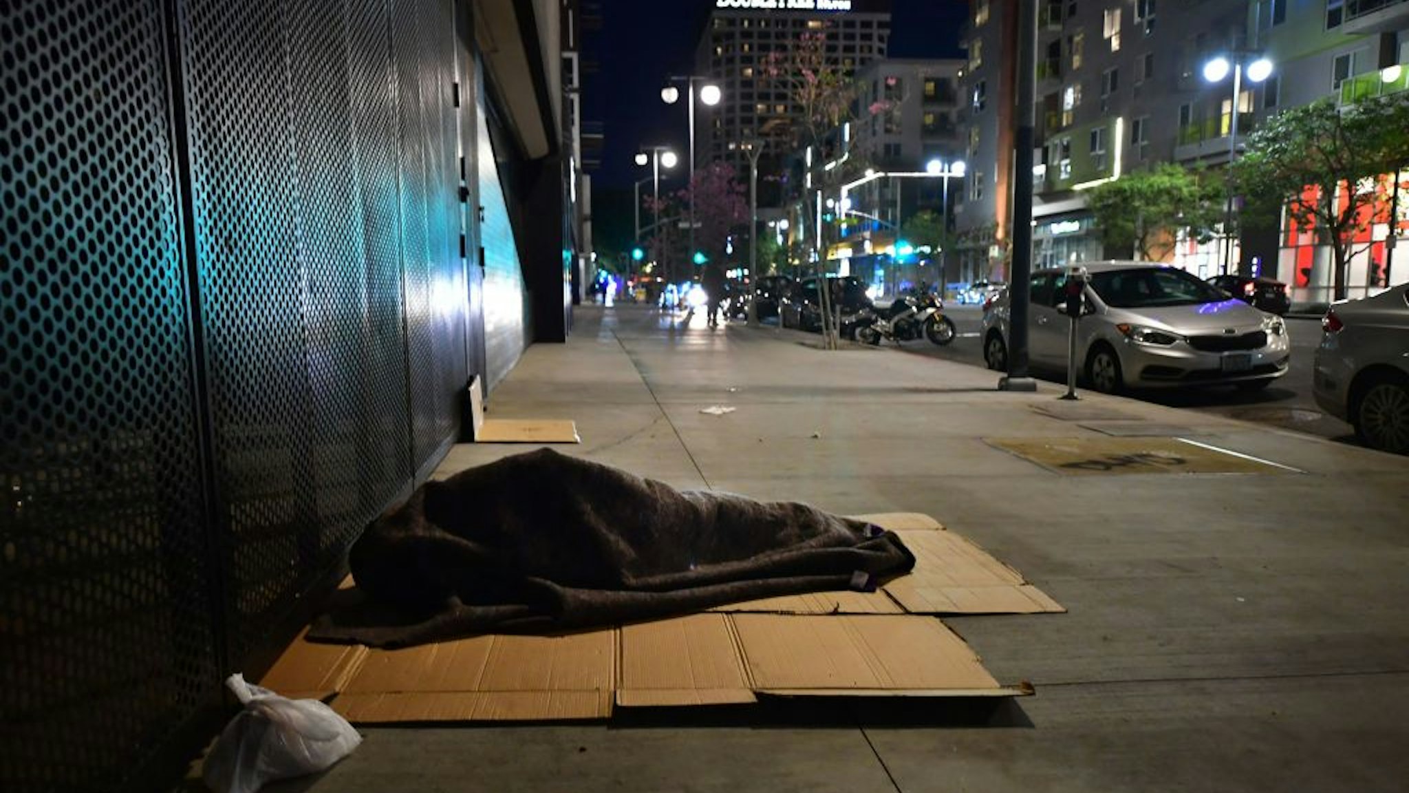 A homeless person sleeps covered with a blanket on cardboard in Los Angeles, California on February 24, 2022, as volunteers participate on the third night of the Greater Los Angeles Homeless Count on February 24, 2022 in Los Angeles, California.