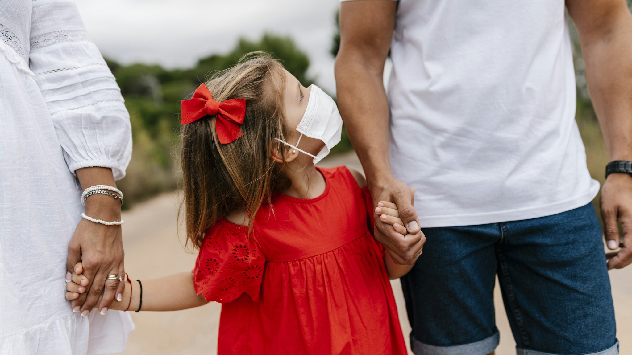Girl wearing mask looking at father while holding hands on country road - stock photo