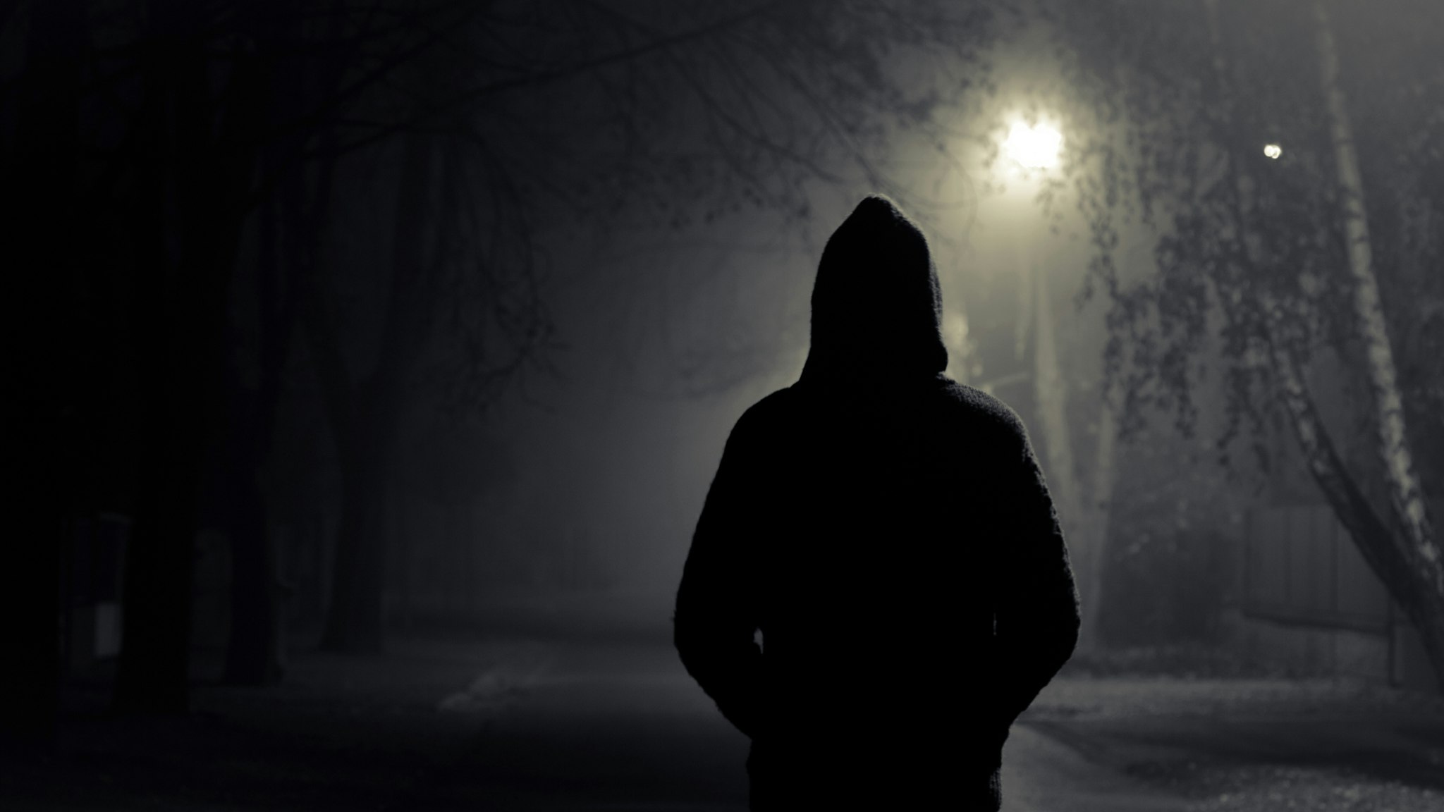 Silhouette of hooded person with spooky dark background - stock photo