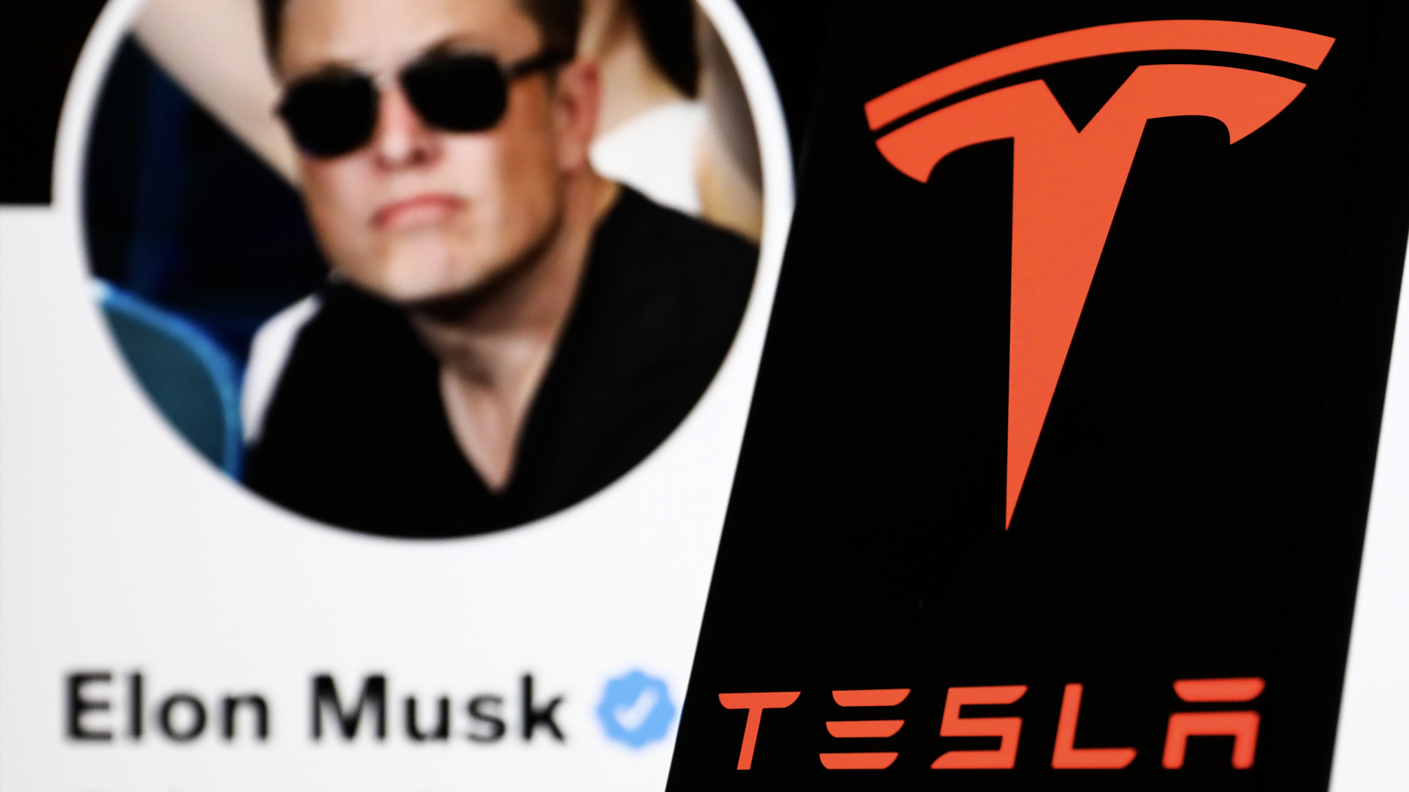 Tesla logo displayed on a phone screen and Elon Musk's Twitter account displayed on a screen in the background are seen in this illustration photo taken in Poland on April 24, 2022.