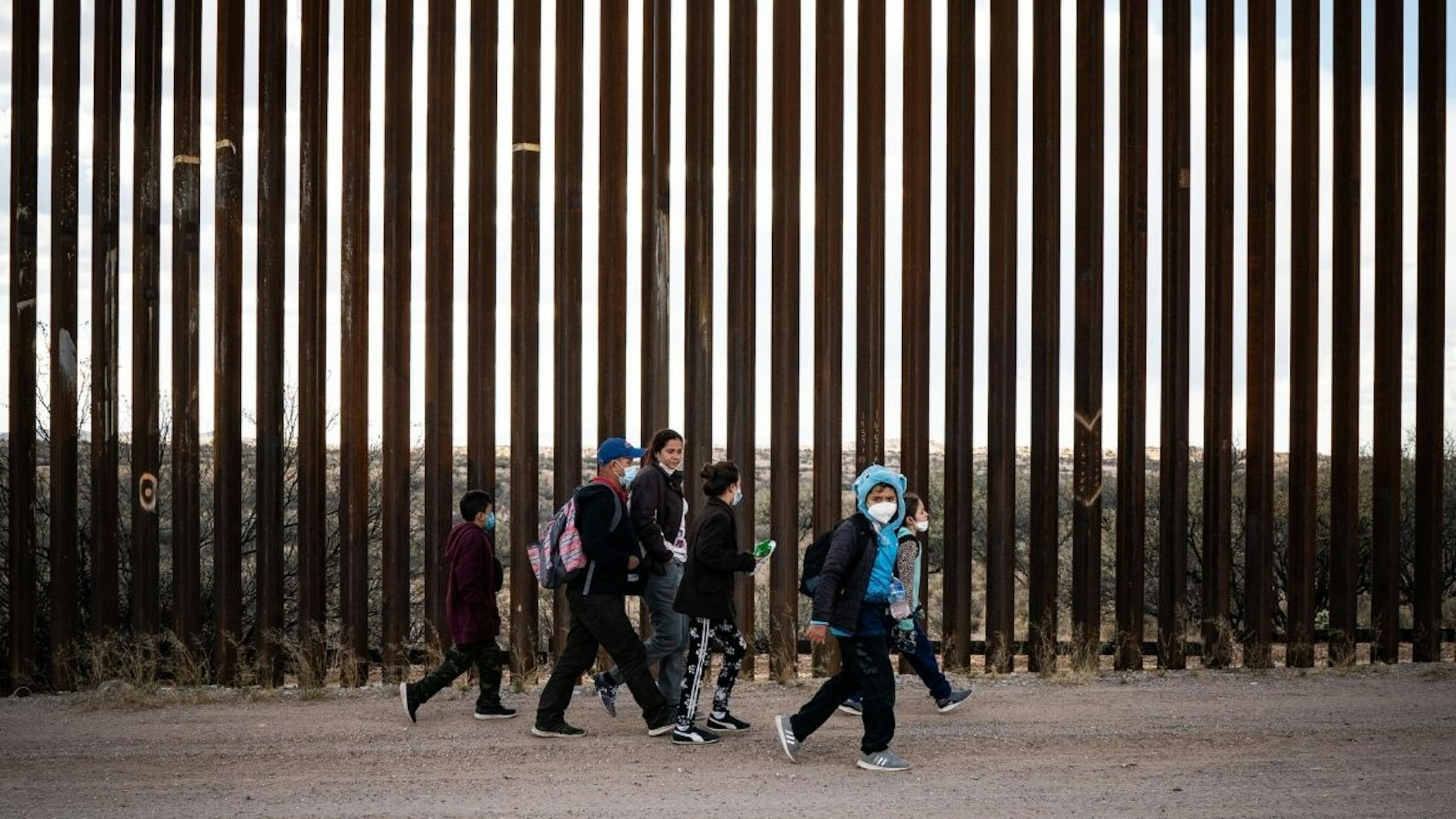 A group of migrant families from Central America walk along side the border wall between the U.S. and Mexico after crossing in to the U.S. near the city of Sasabe, Arizona, Sunday, January 23, 2022.