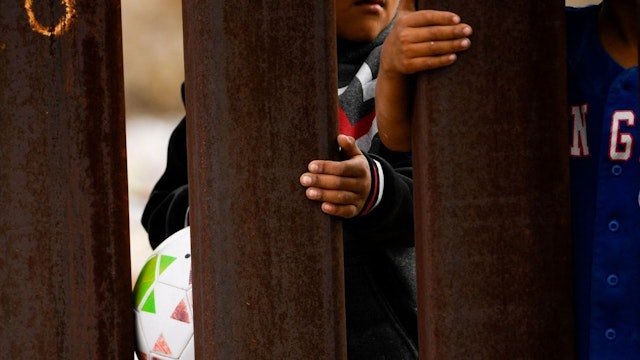 Children hold on to a border wall fence from the Mexico side of the US-Mexico border between New Mexico and Chihuahua state on December 9, 2021 in Sunland Park, New Mexico.