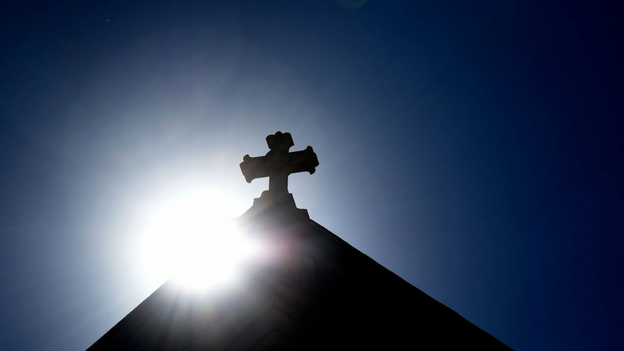 SANTA FE, NEW MEXICO - JUNE 21, 2020: The sun rises behind a stone cross atop the historic Cathedral Basilica of St. Frances of Assisi in Santa Fe, New Mexico.