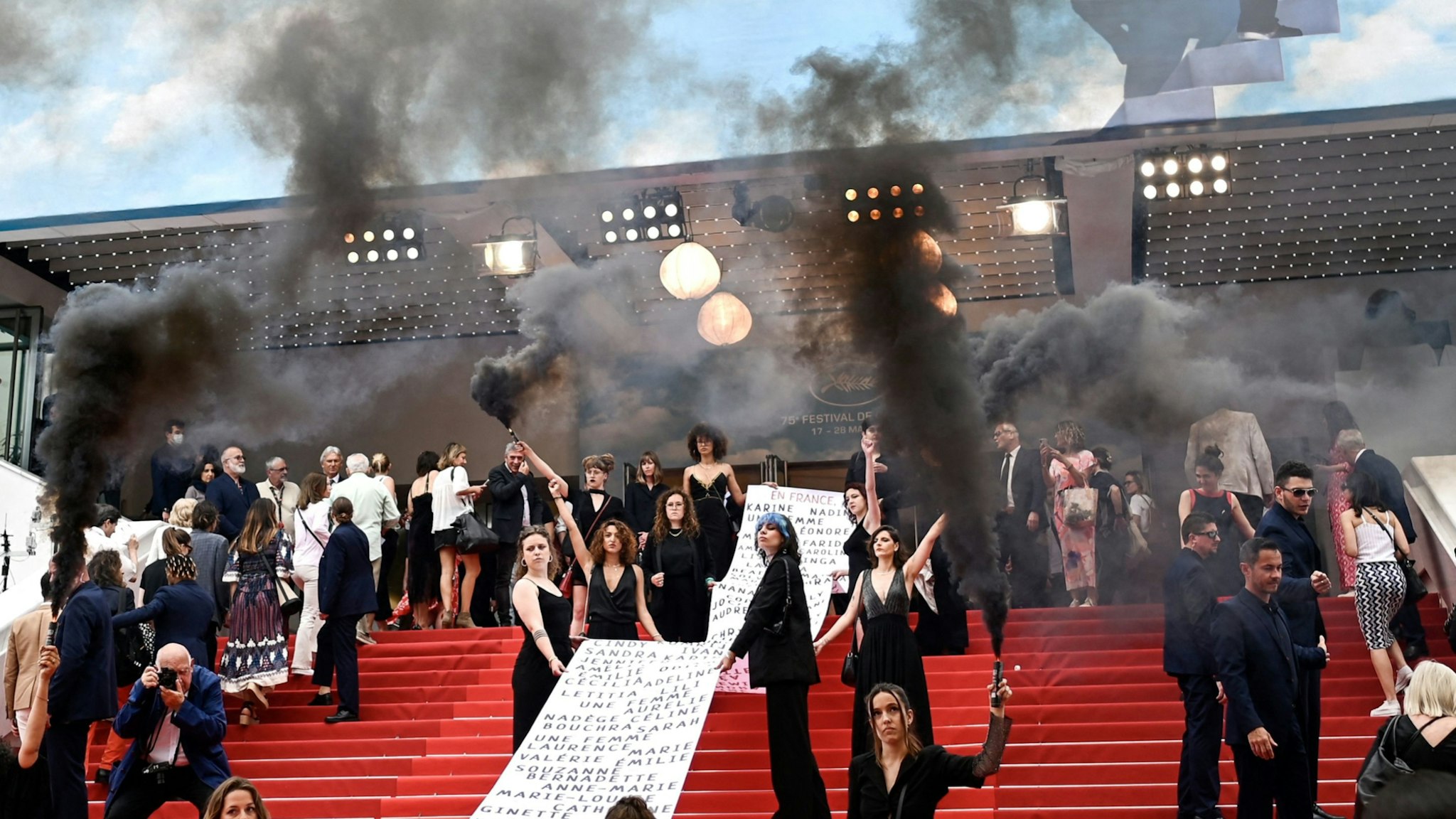 French photographer Raymond Depardon (3rdR) takes photos of members of the feminist movement "Les Colleuses" holding a banner bearing the names of 129 women who died as a result of domestic violence since the last Cannes Film Festival, before the screening of the film "Holy Spider" during the 75th edition of the Cannes Film Festival in Cannes, southern France, on May 22, 2022.