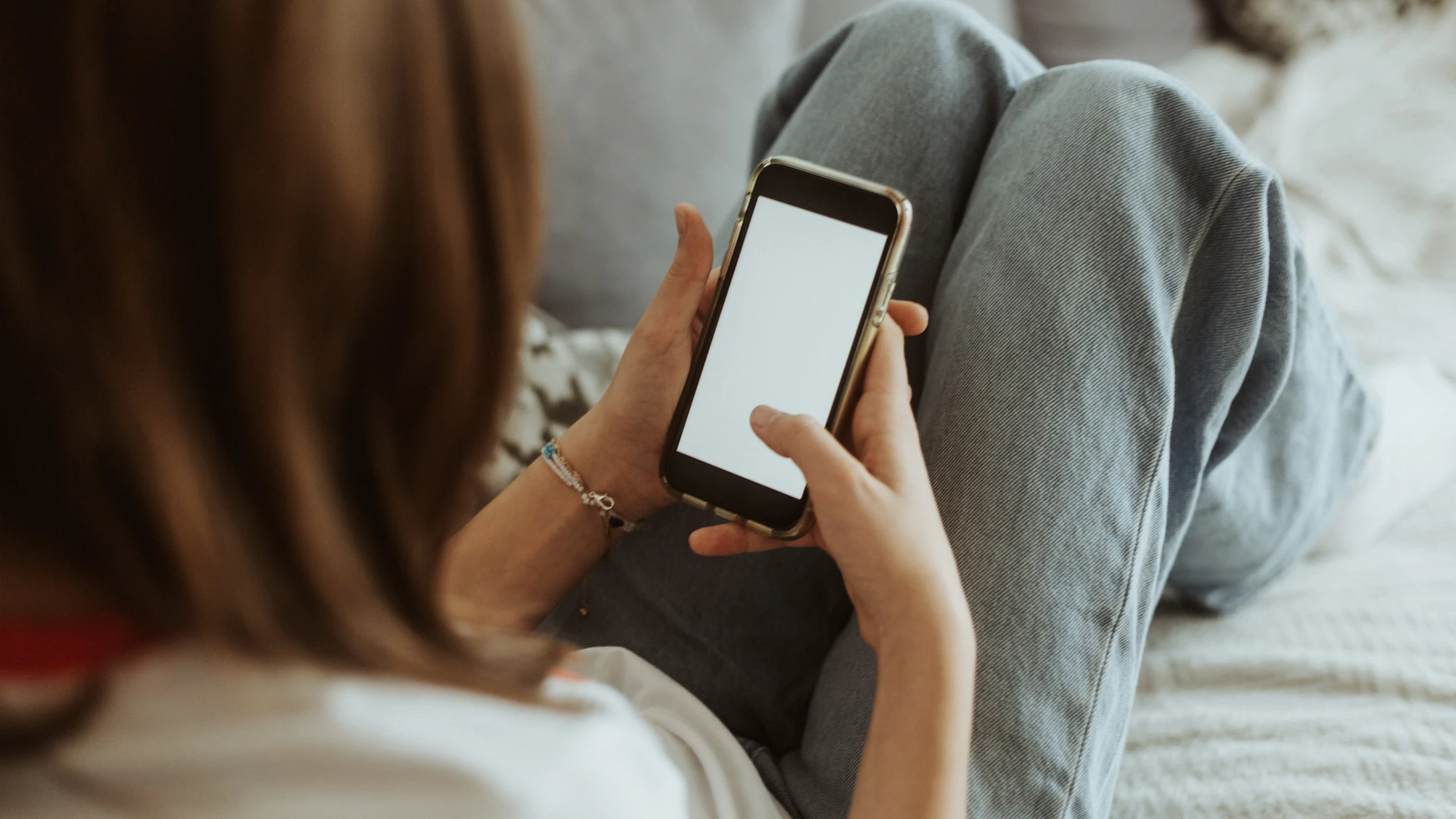 Close-up of a 12 year old girl laying on a couch holding a mobile phone with a blank screen in hands.