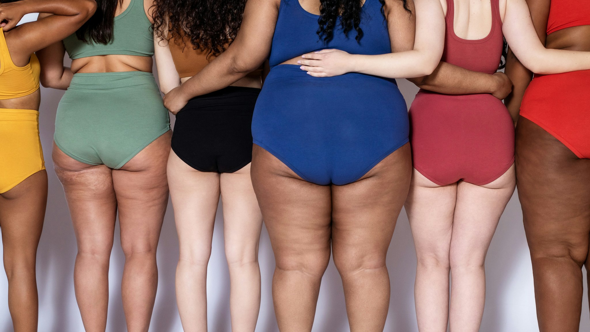 Rear view of group of women with different body type in underwear standing together on white background.