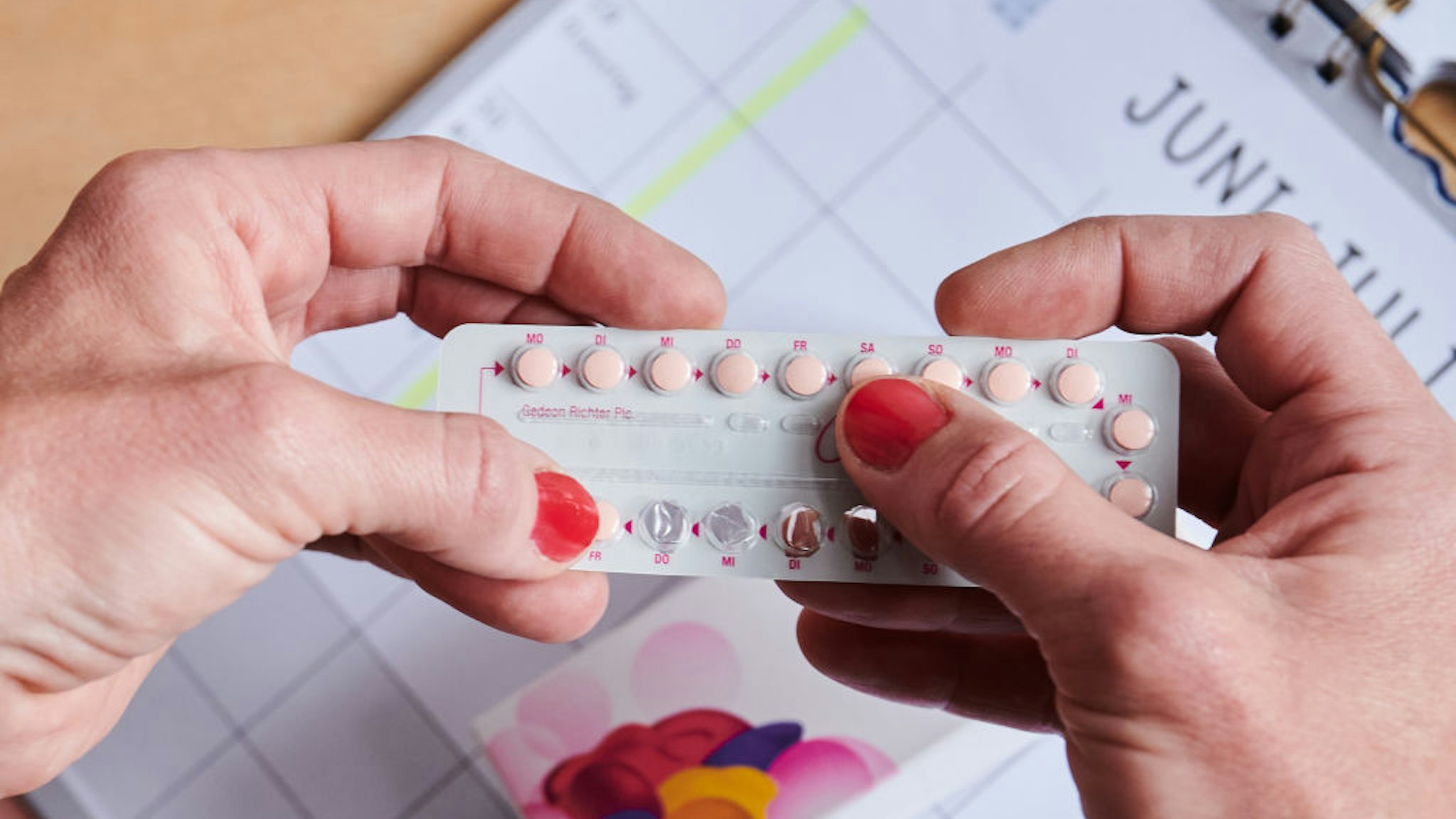SYMBOL - 25 May 2021, Berlin: Above a calendar, a woman takes the next pill from the monthly pack of the contraceptive pill. The contraceptive pill went on sale in Germany 60 years ago. (to dpa "Myth and milestone - 60 years of the pill in Germany ") Photo: Annette Riedl/dpa (Photo by Annette Riedl/picture alliance via Getty Images)