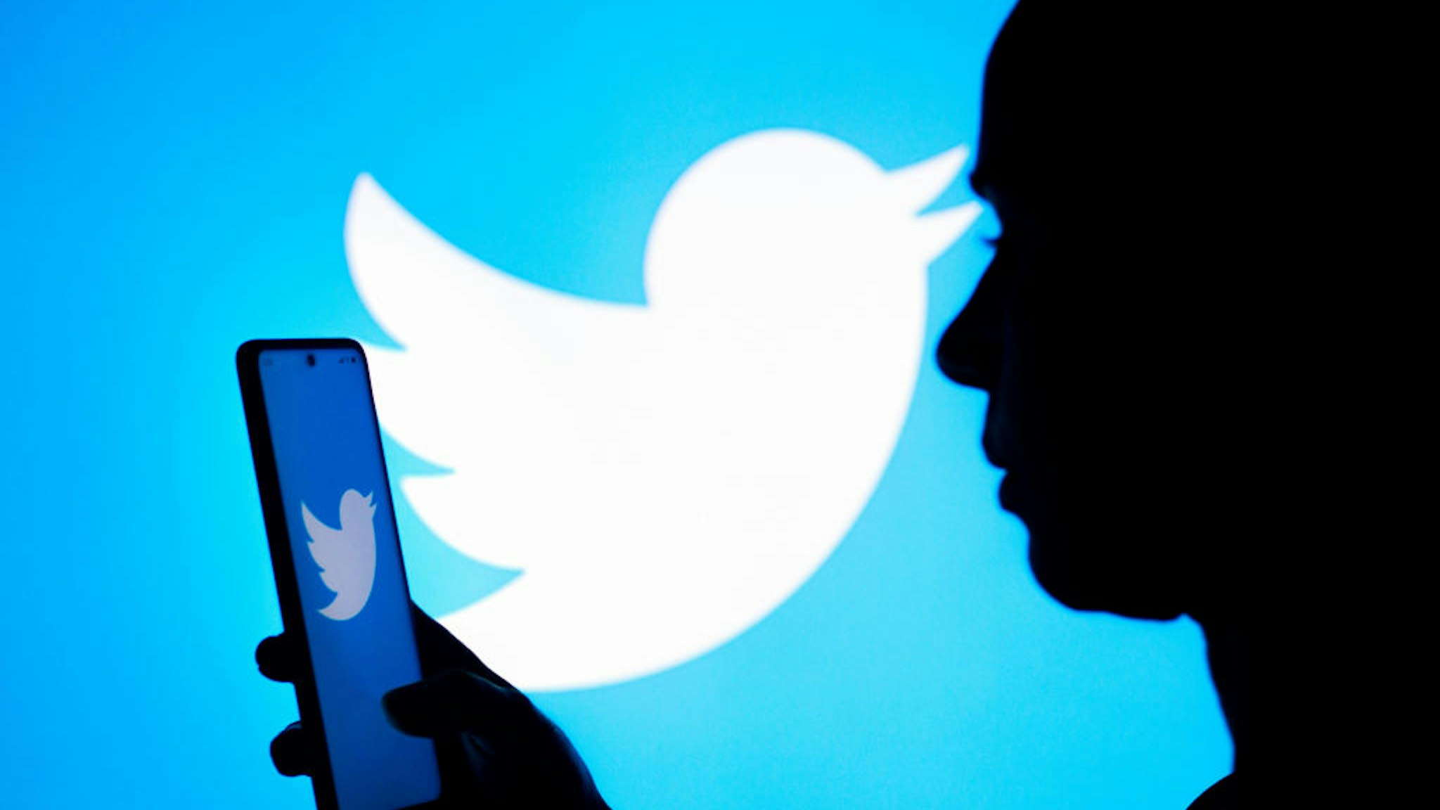 BRAZIL - 2022/03/21: In this photo illustration, a woman's silhouette holds a smartphone with the Twitter logo displayed on the screen and in the background. (Photo Illustration by Rafael Henrique/SOPA Images/LightRocket via Getty Images)