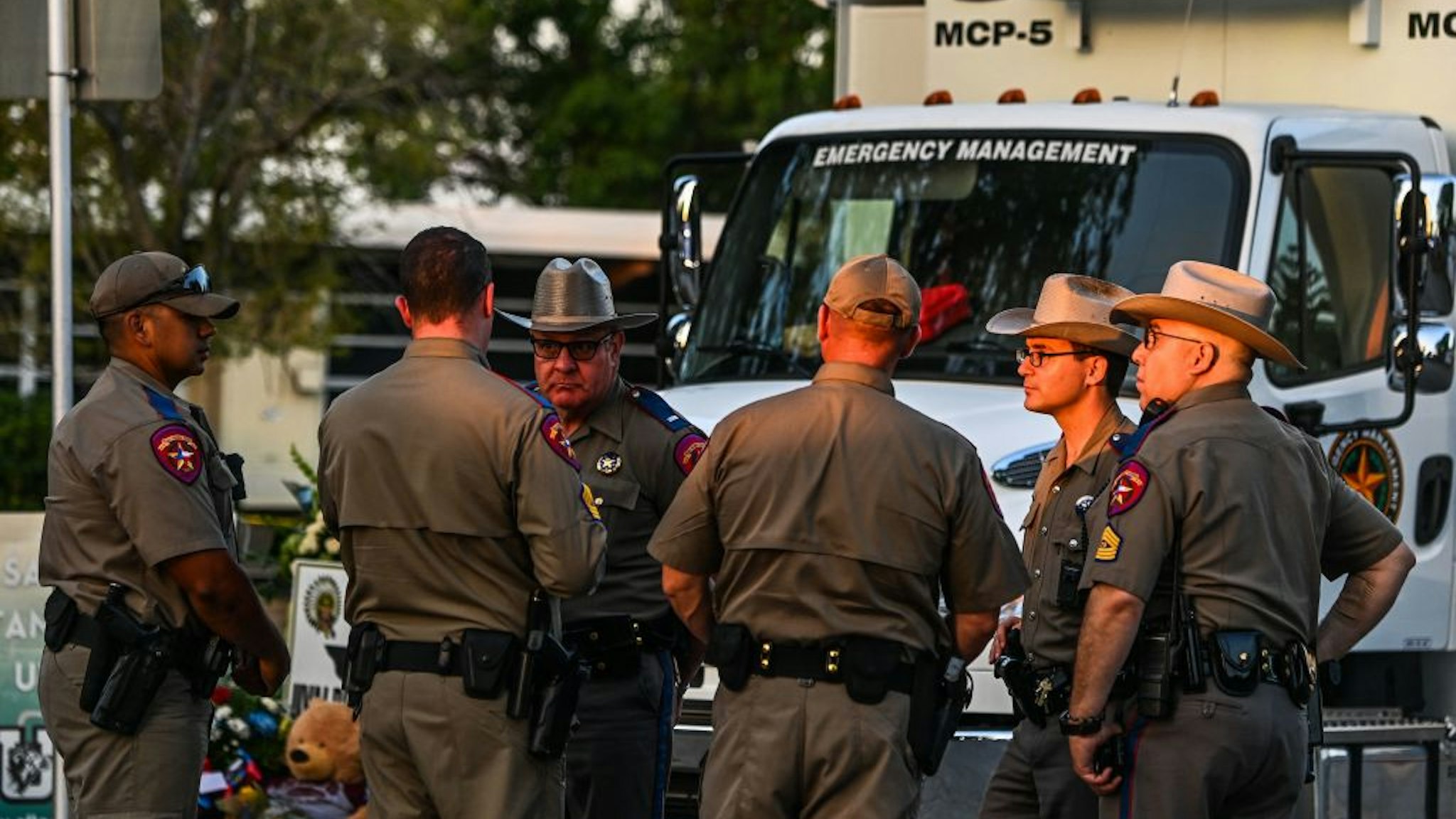 Police officers speak near a makeshift memorial for the shooting victims outside Robb Elementary School in Uvalde, Texas, on May 27, 2022. - Texas police faced angry questions May 26, 2022 over why it took an hour to neutralize the gunman who murdered 19 small children and two teachers in Uvalde, as video emerged of desperate parents begging officers to storm the school. (Photo by CHANDAN KHANNA / AFP) (Photo by CHANDAN KHANNA/AFP via Getty Images)