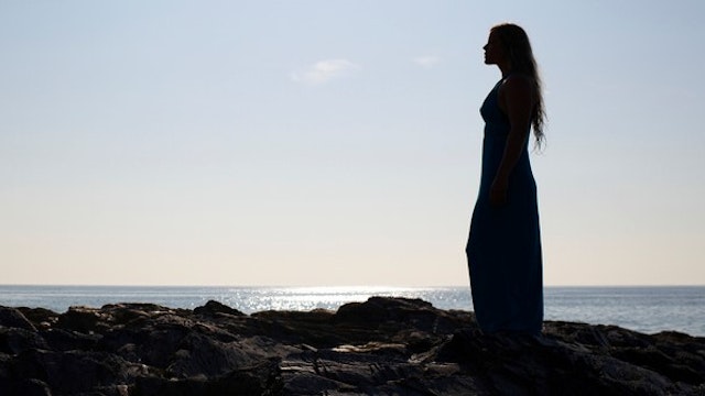 Silhouette of woman in dress against seascape.