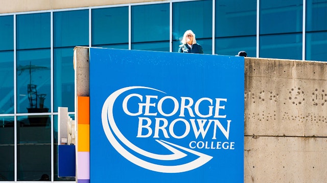 Woman smoking at George Brown college's concrete balcony, with schools logo on the outside wall.