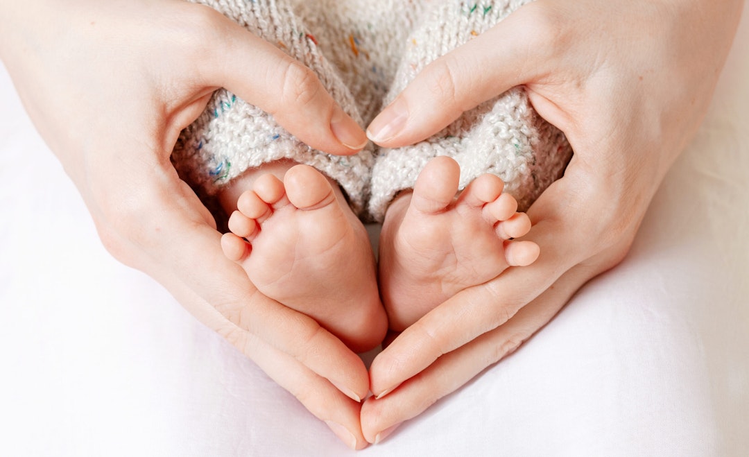 Hands in the shape of a heart around tiny baby feet