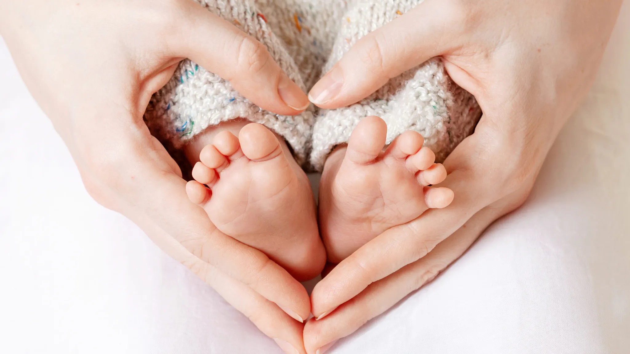 Baby feet in mother hands. Tiny Newborn Baby’s feet on female Heart Shaped hands closeup. Mom and her Child. Happy Family concept. Beautiful conceptual image of Maternity mom and baby