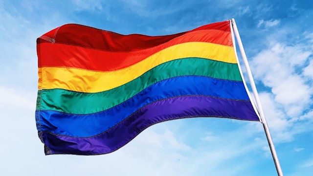 Rainbow flag waving in the wind against blue sky - stock photo