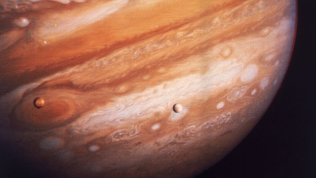 Jupiter, the largest planet in our solar system, with two of its satellites, Io on the left (above Jupiter's Great Red Spot) and Europa on the right, March 1979. The image was taken by the Voyager 1 spacecraft.